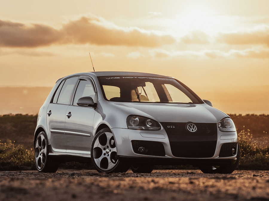 A silver volkswagen golf is parked on a dirt road at sunset.