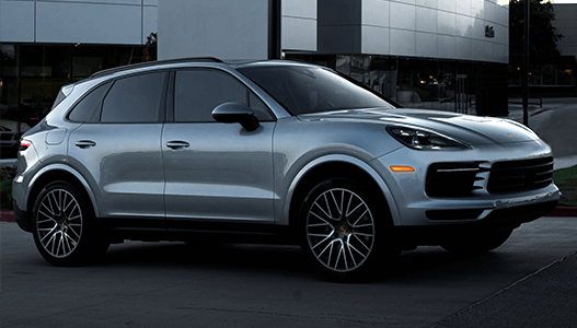A silver porsche cayenne is parked in front of a building.