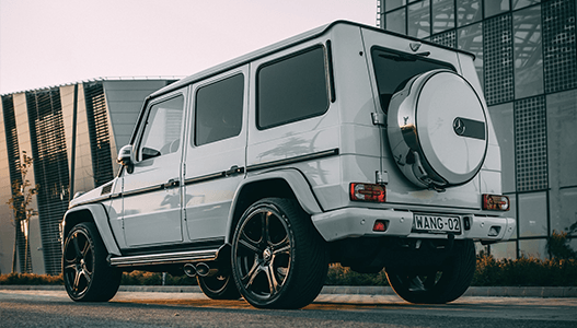 A white mercedes benz g class is parked on the side of the road in front of a building.
