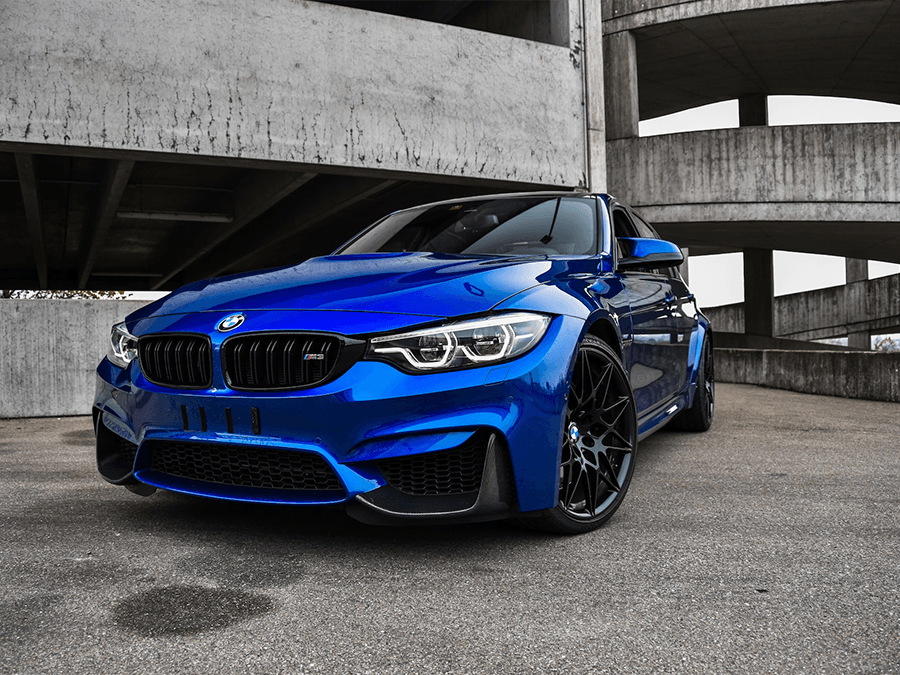 A blue bmw m3 is parked in front of a concrete building.