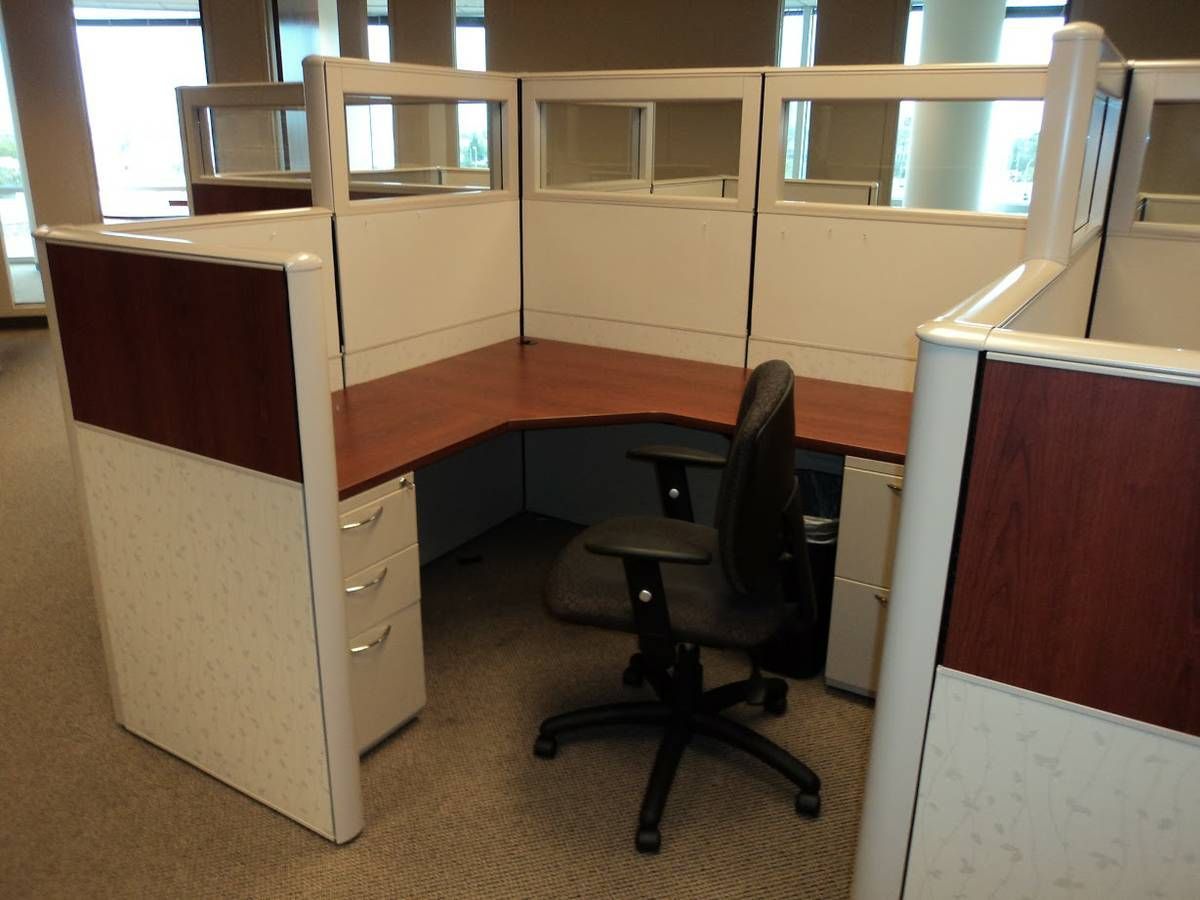 Office cubicle with L-shaped desk, black chair, and white and wood paneling.