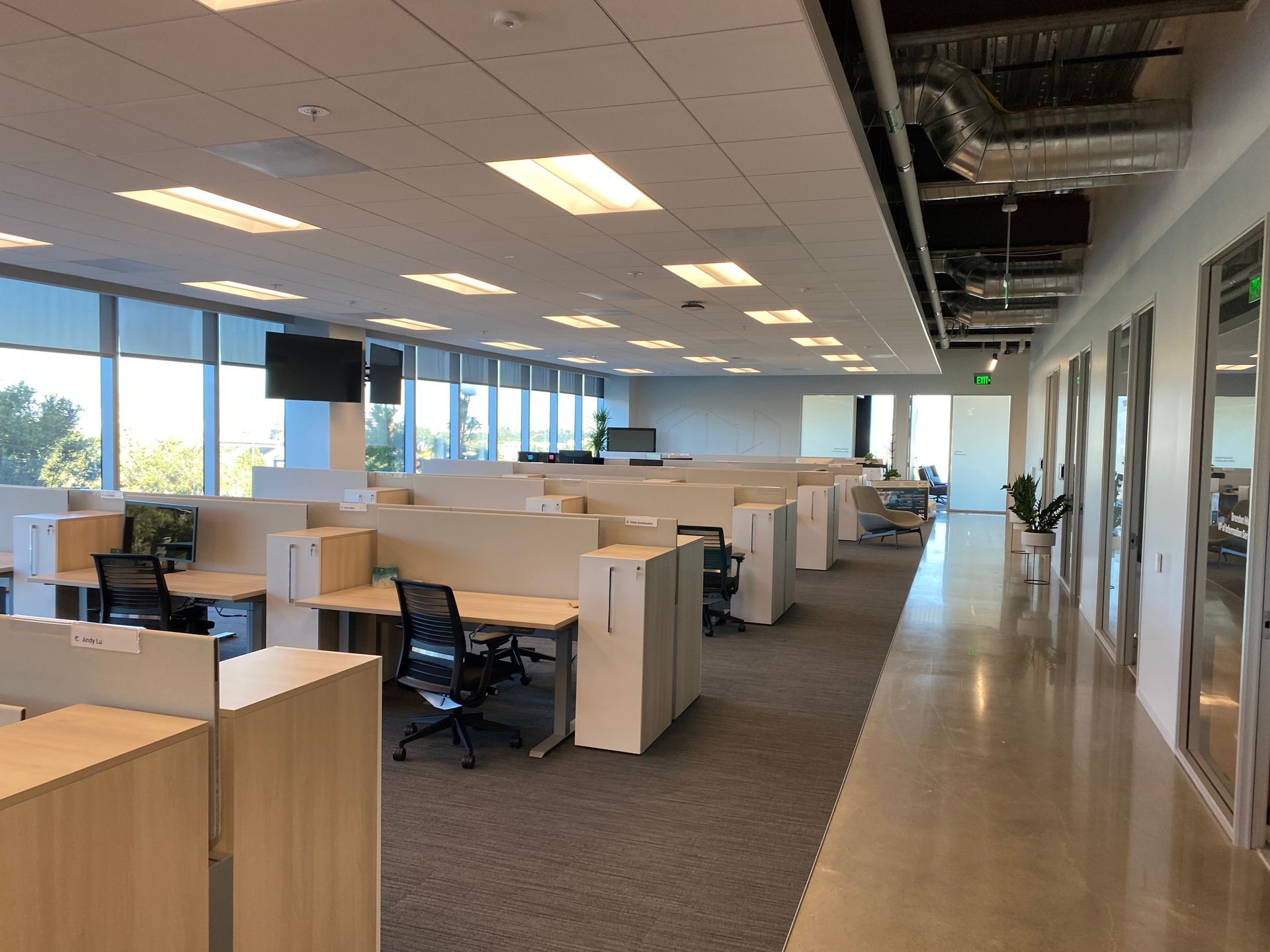 Open office with rows of cubicles, desks, and chairs under bright ceiling light.
