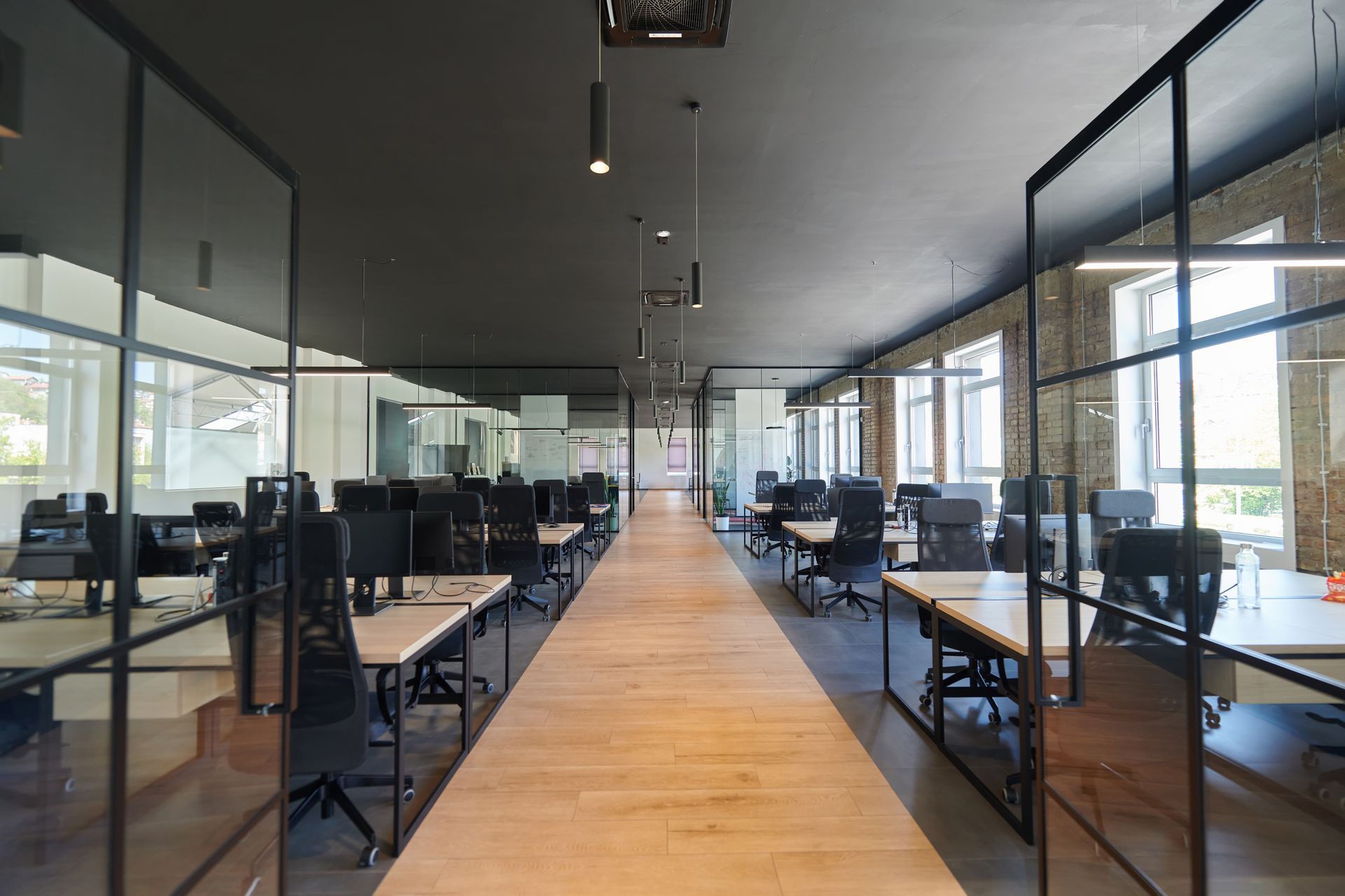 Modern office with glass cubicles, desks, chairs, and bright natural light throughout workspace.