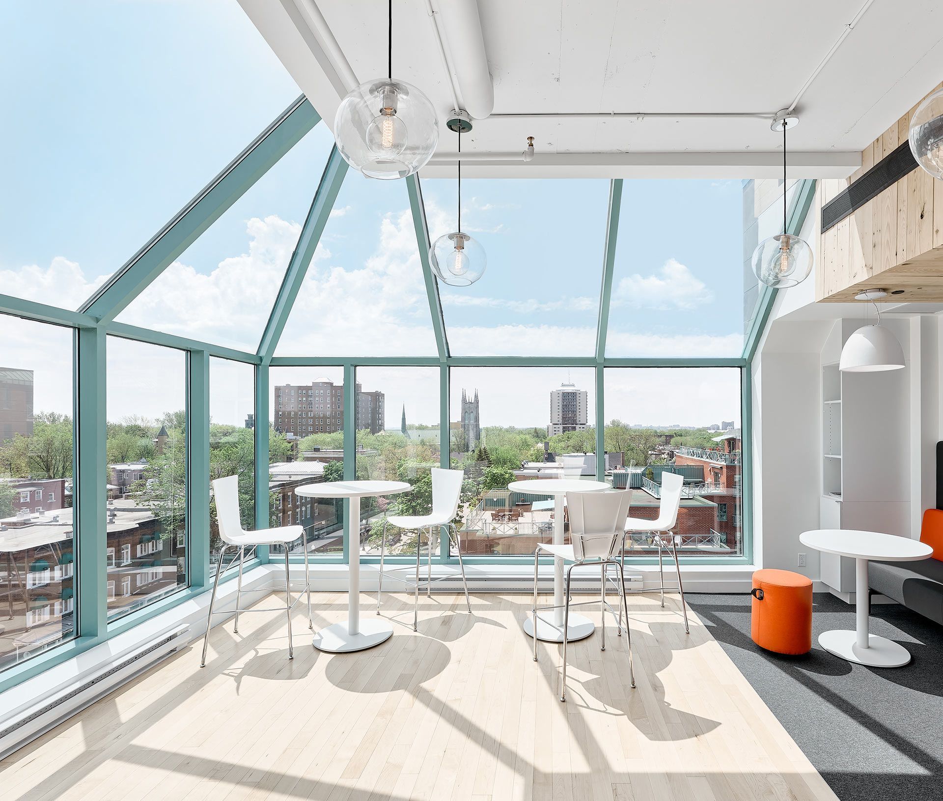 Bright office lounge with large windows, white tables/chairs, city view, sunny day.
