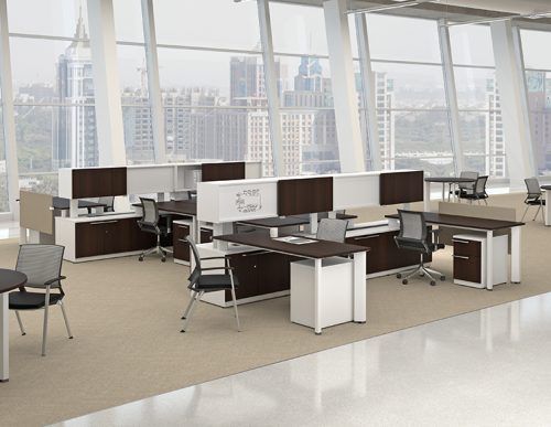Modern office space with desks, chairs, and city view through large windows. Brown and white furniture, beige carpet.