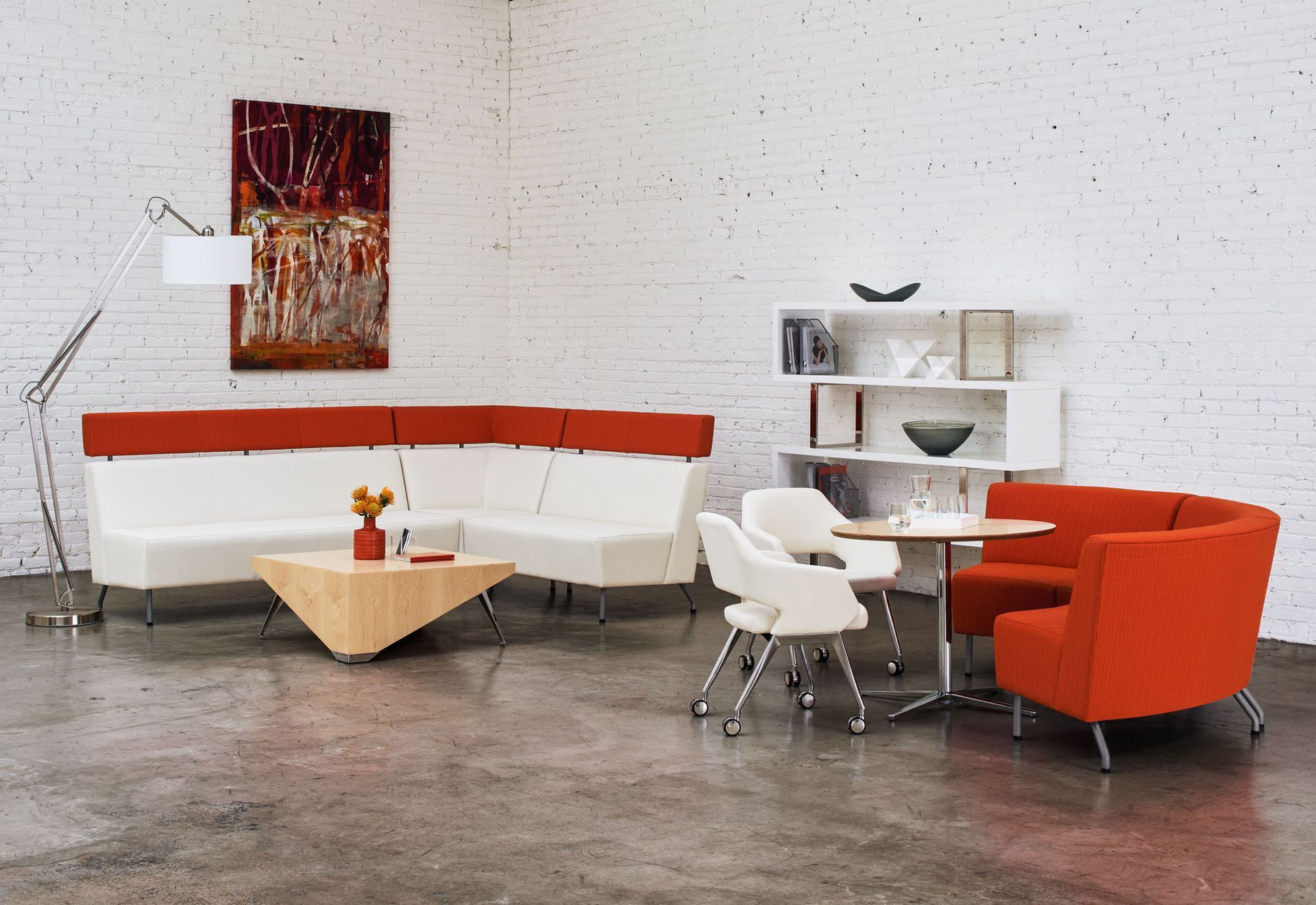 Modern office lounge with white and orange seating, art, and minimalist furniture.