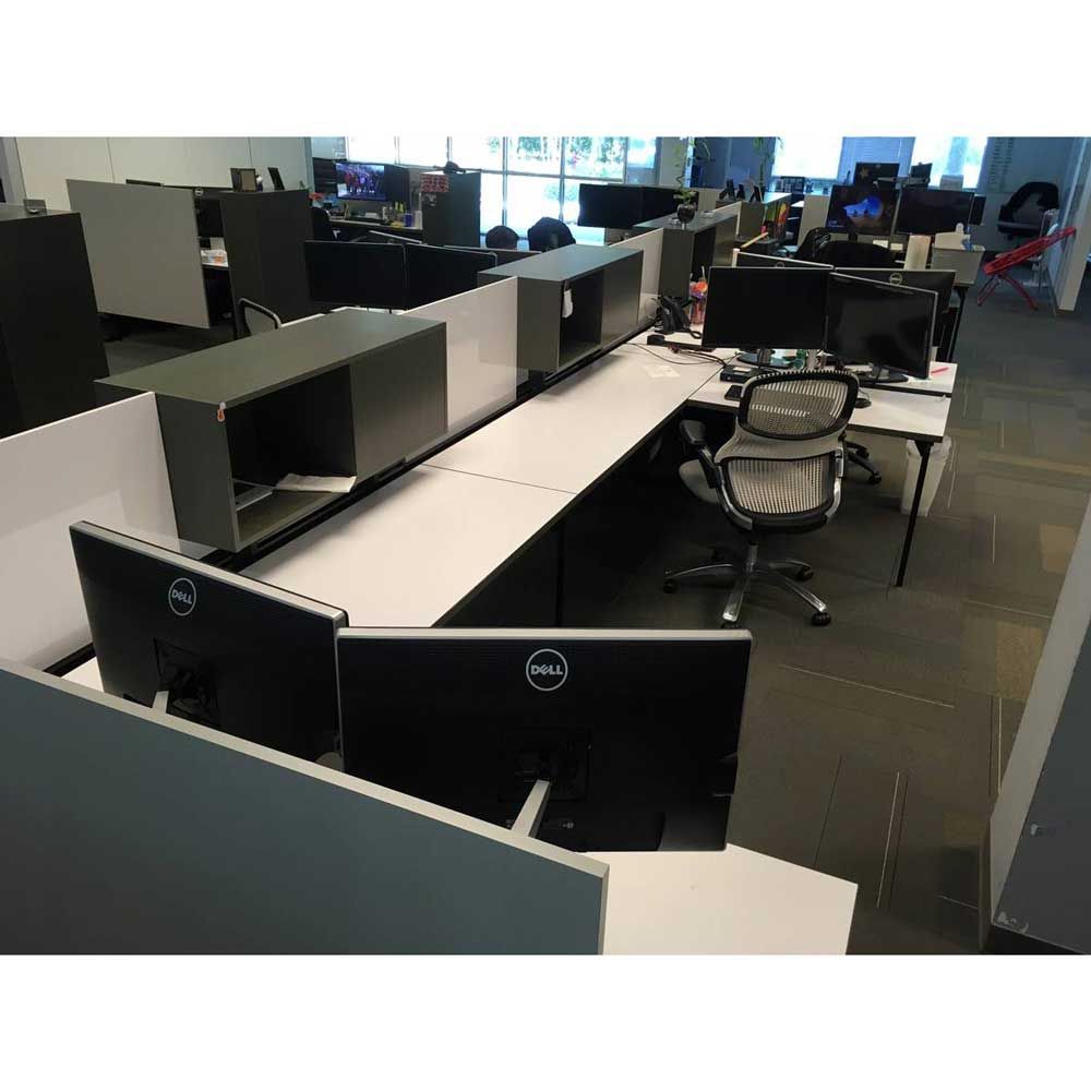 Office cubicles with computers, screens, and chairs. White and gray furniture.