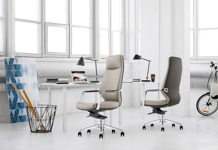 Two office chairs with desks, a bicycle, and artwork in a bright room with windows.