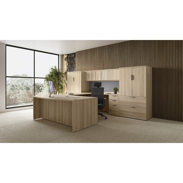 A modern office with a light wood desk, cabinets, and large window overlooking a snowy landscape.