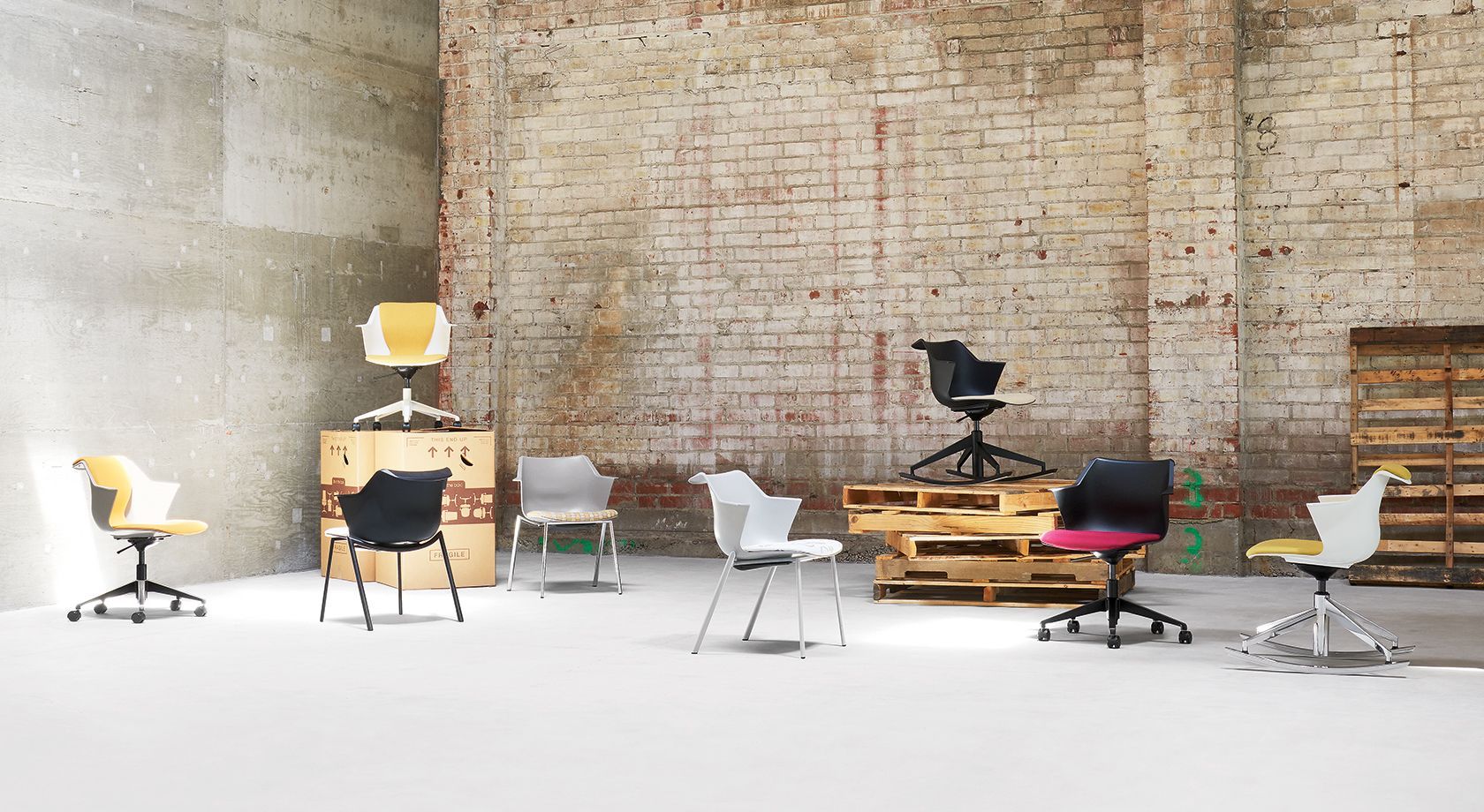 Office chairs of various colors arranged in an industrial setting with brick and concrete walls.