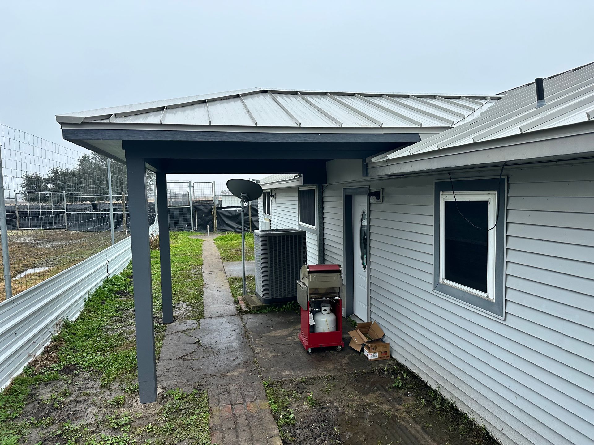 Exterior view of a house with a covered walkway and metal roof. A propane tank and equipment are present.