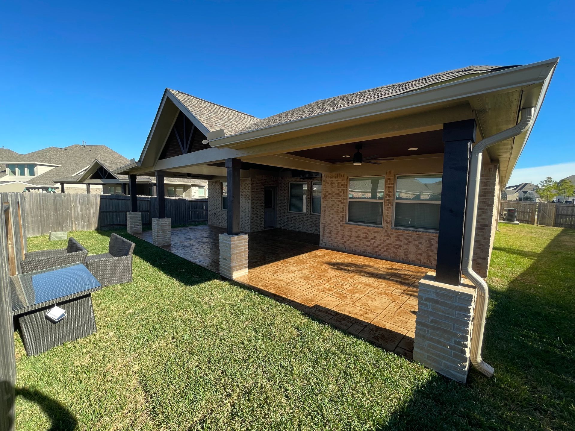 Backyard patio with brick columns, wood ceiling, and brown stained concrete floor.  Green grass and blue sky.