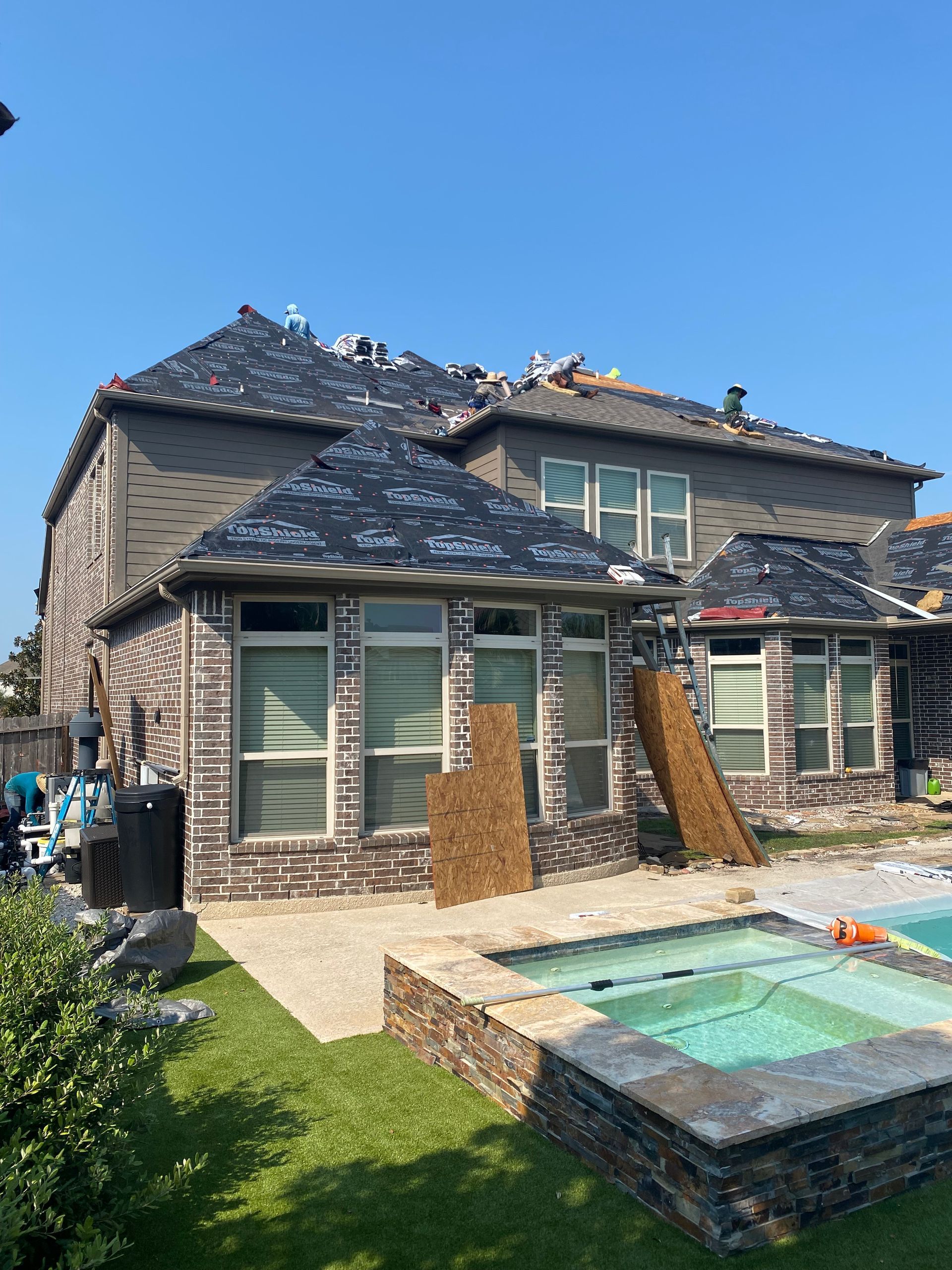 House with brick exterior and partially replaced roof, overlooking a backyard with pool.