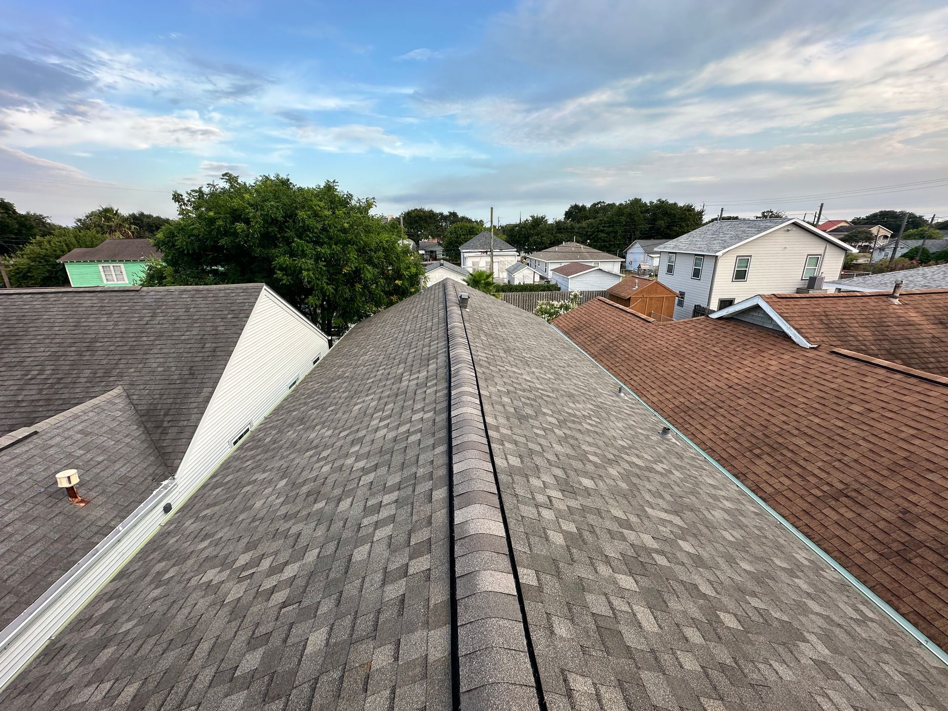 View of residential rooftops with asphalt shingles under a cloudy sky.