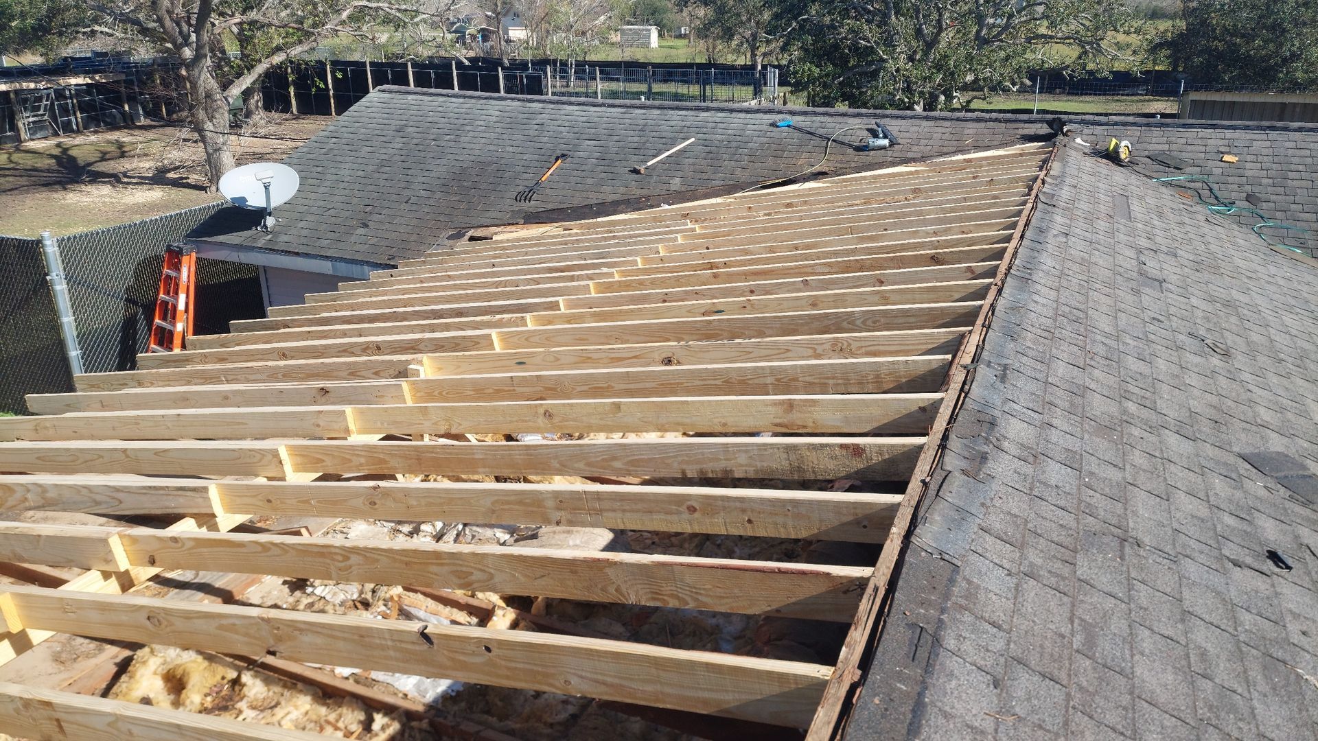 Roof under construction with exposed wooden beams and partially removed shingles.