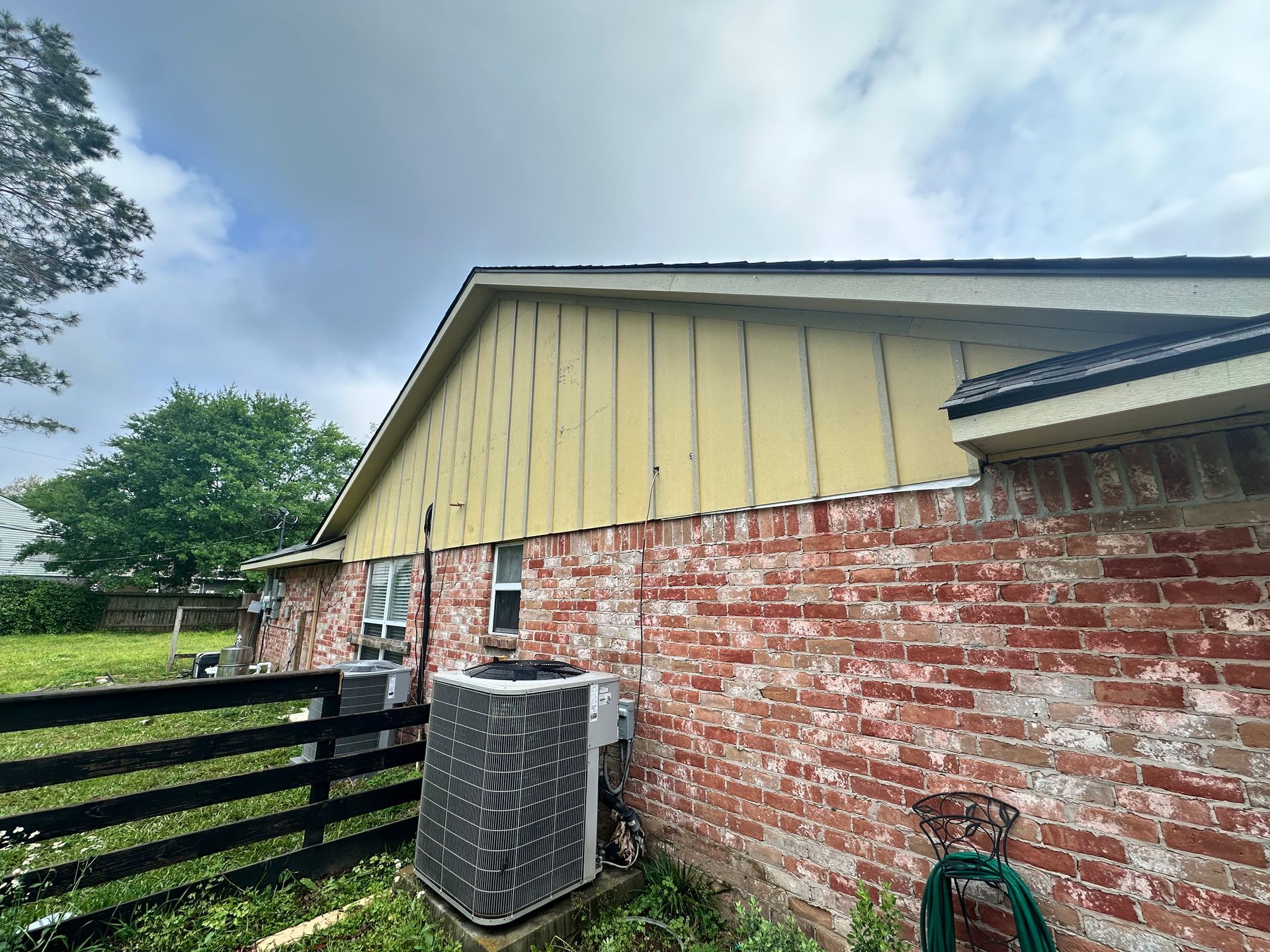 Yellow siding on a house with a red brick exterior, air conditioning units, and a black fence.