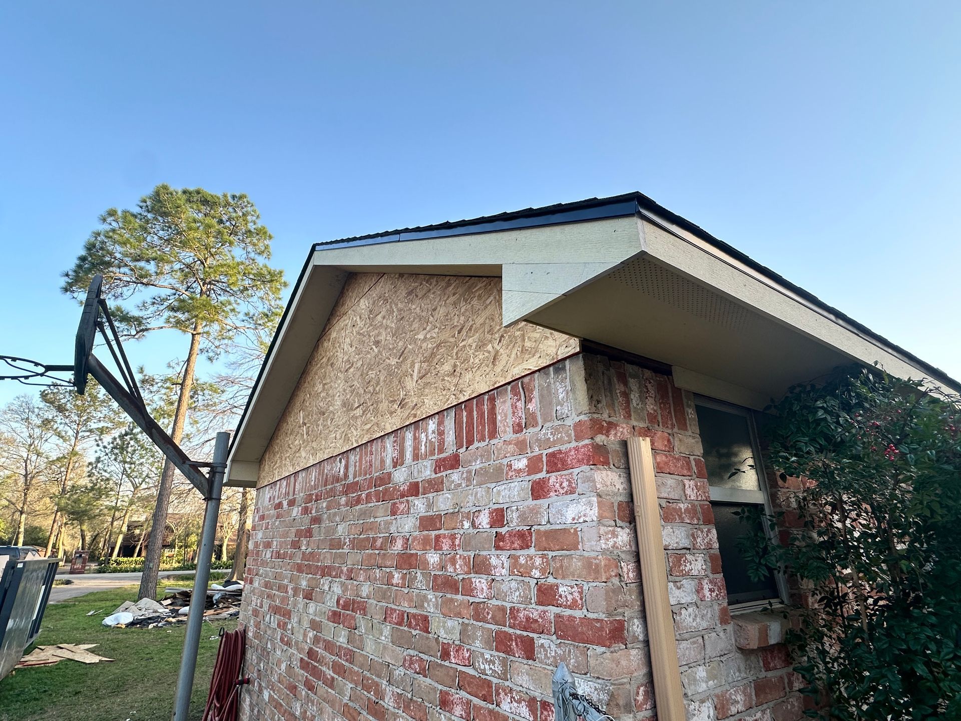 Brick house with exposed wood under new roof, against a blue sky.