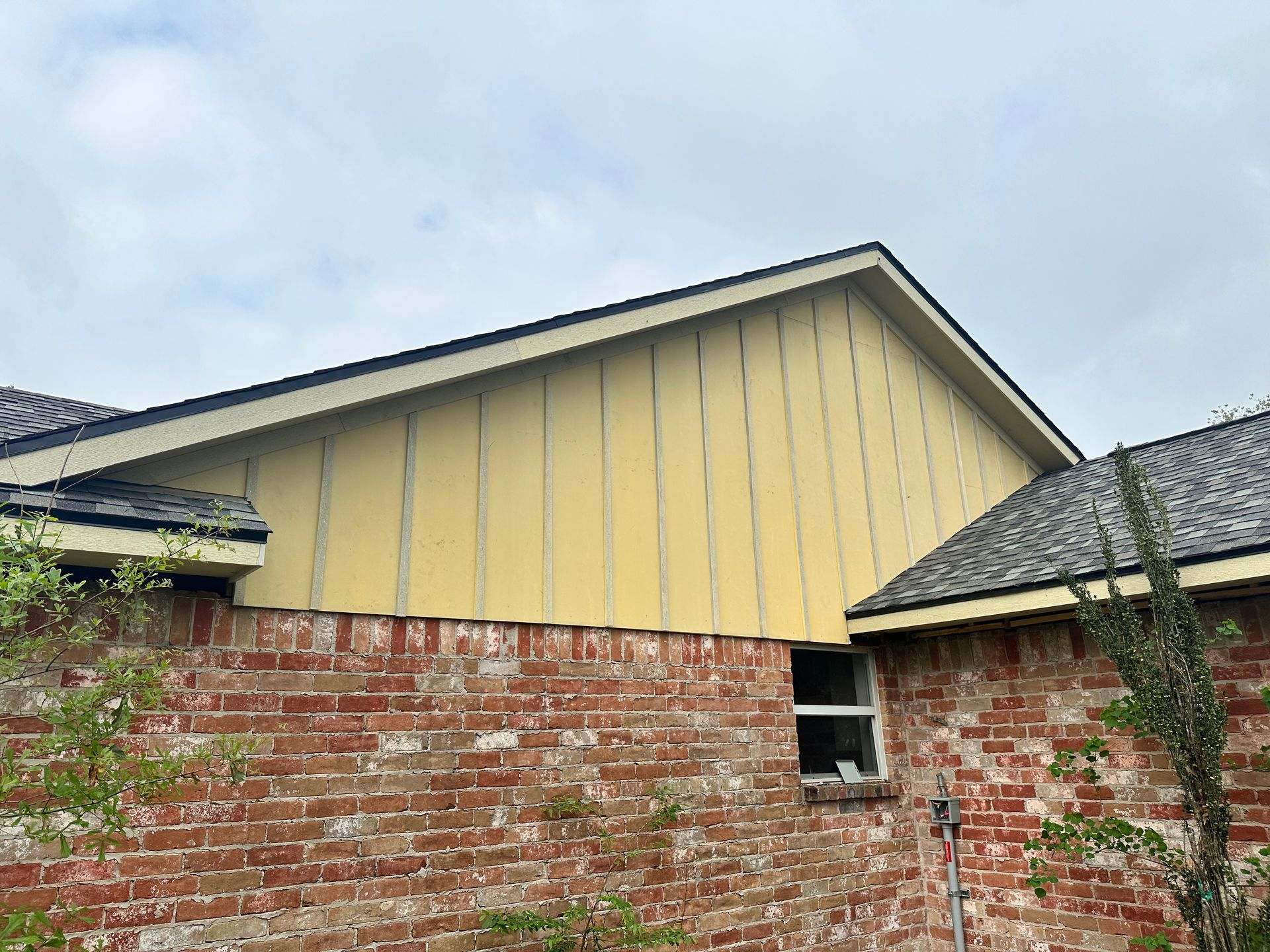 Exterior view of a brick house with yellow siding on a gable roof, and a small window.