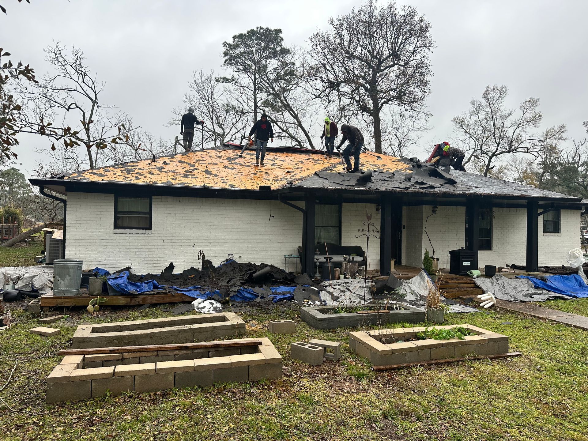 People repairing a roof damaged by a storm; a white house, cloudy day.