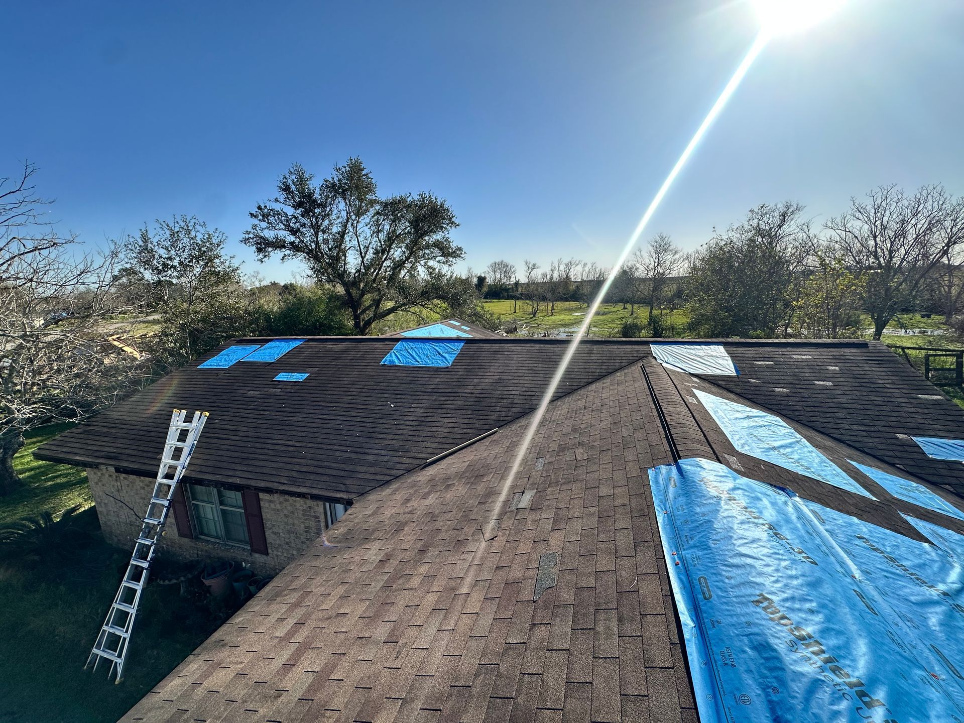 A rooftop with blue tarps, ladder, and a sunny sky.