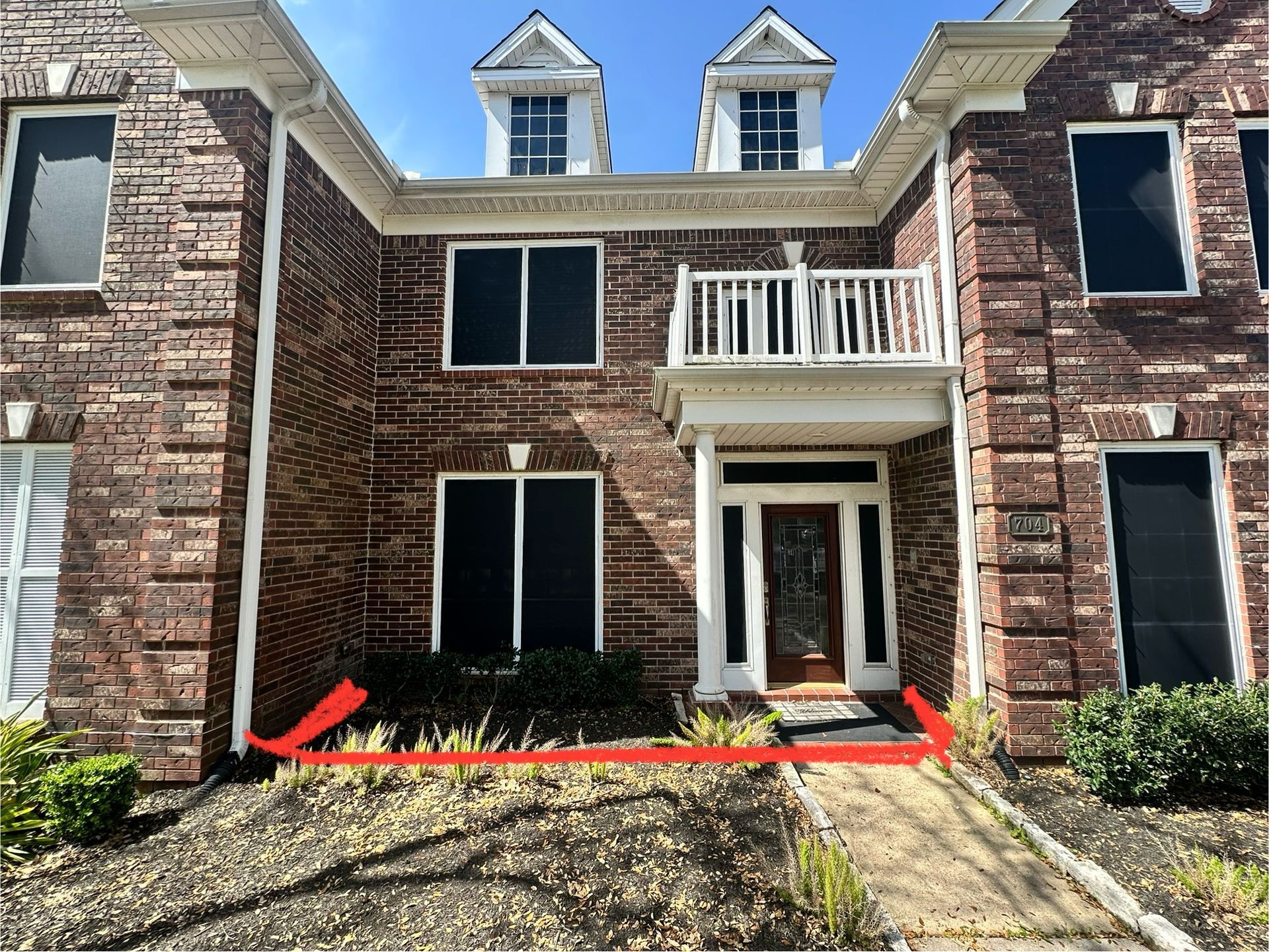 Two-story brick house with a front porch. A low garden bed is in front, and a sidewalk leads to the door.