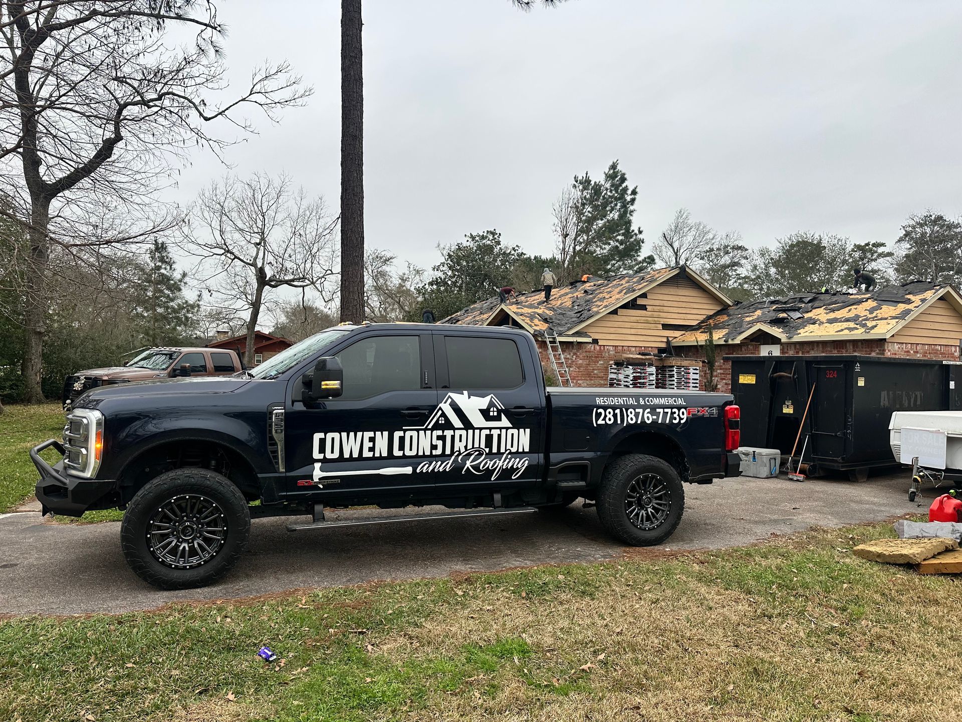 Dark blue Cowen Construction truck parked in front of a house with roof replacement in progress.