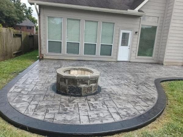 Concrete patio with fire pit, and house in the background. Grass surrounds the patio.