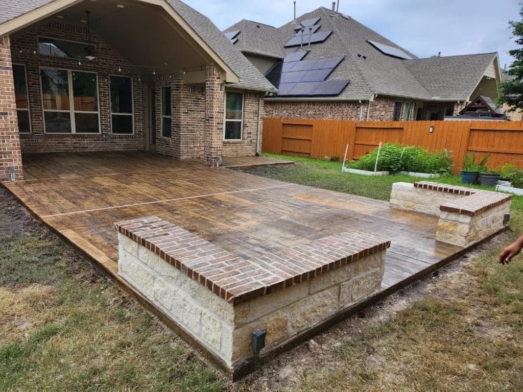 Backyard patio with brick and stone features, covered porch, and brown fence.