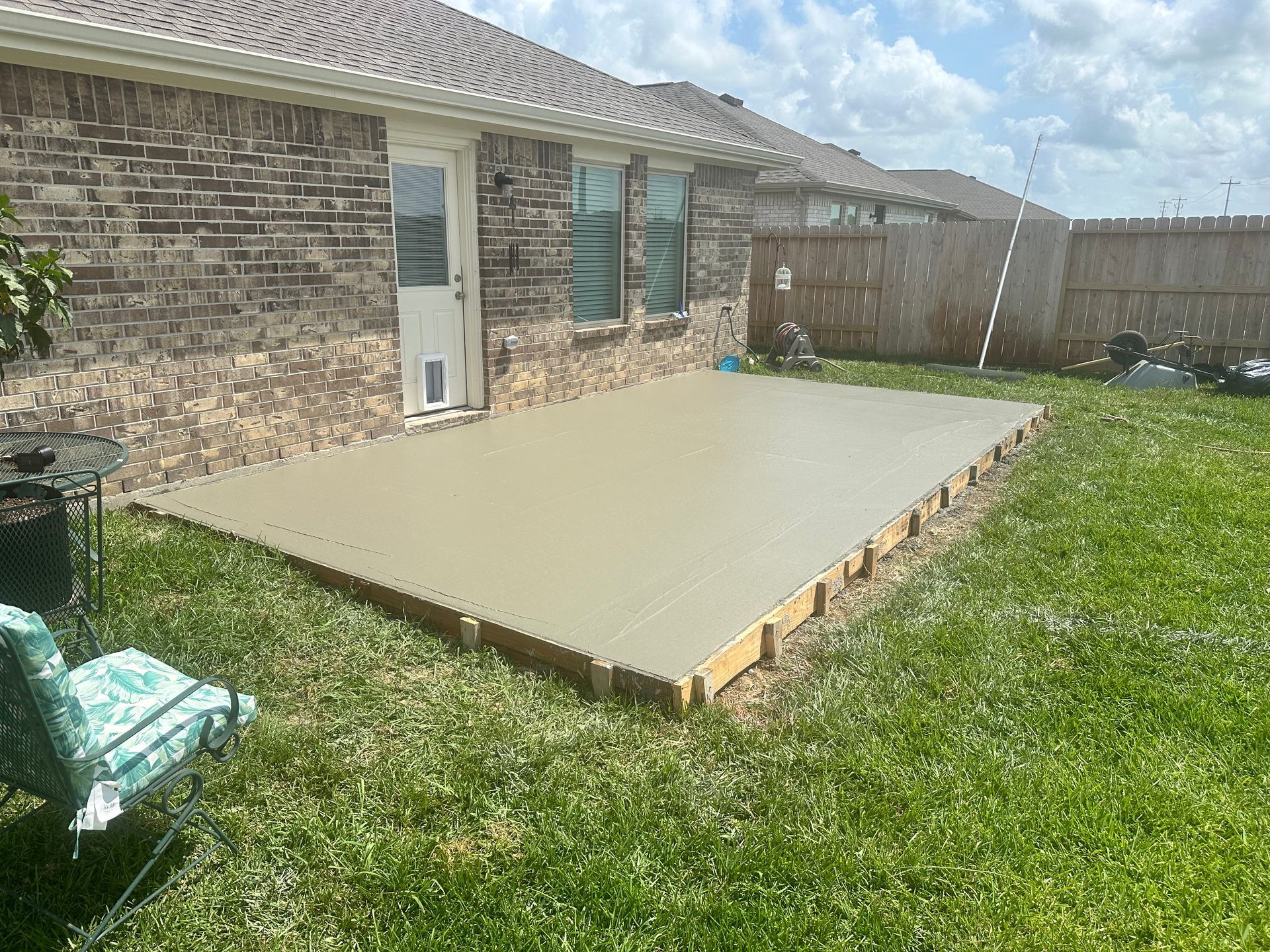 Freshly poured concrete patio in a backyard setting next to a brick house.