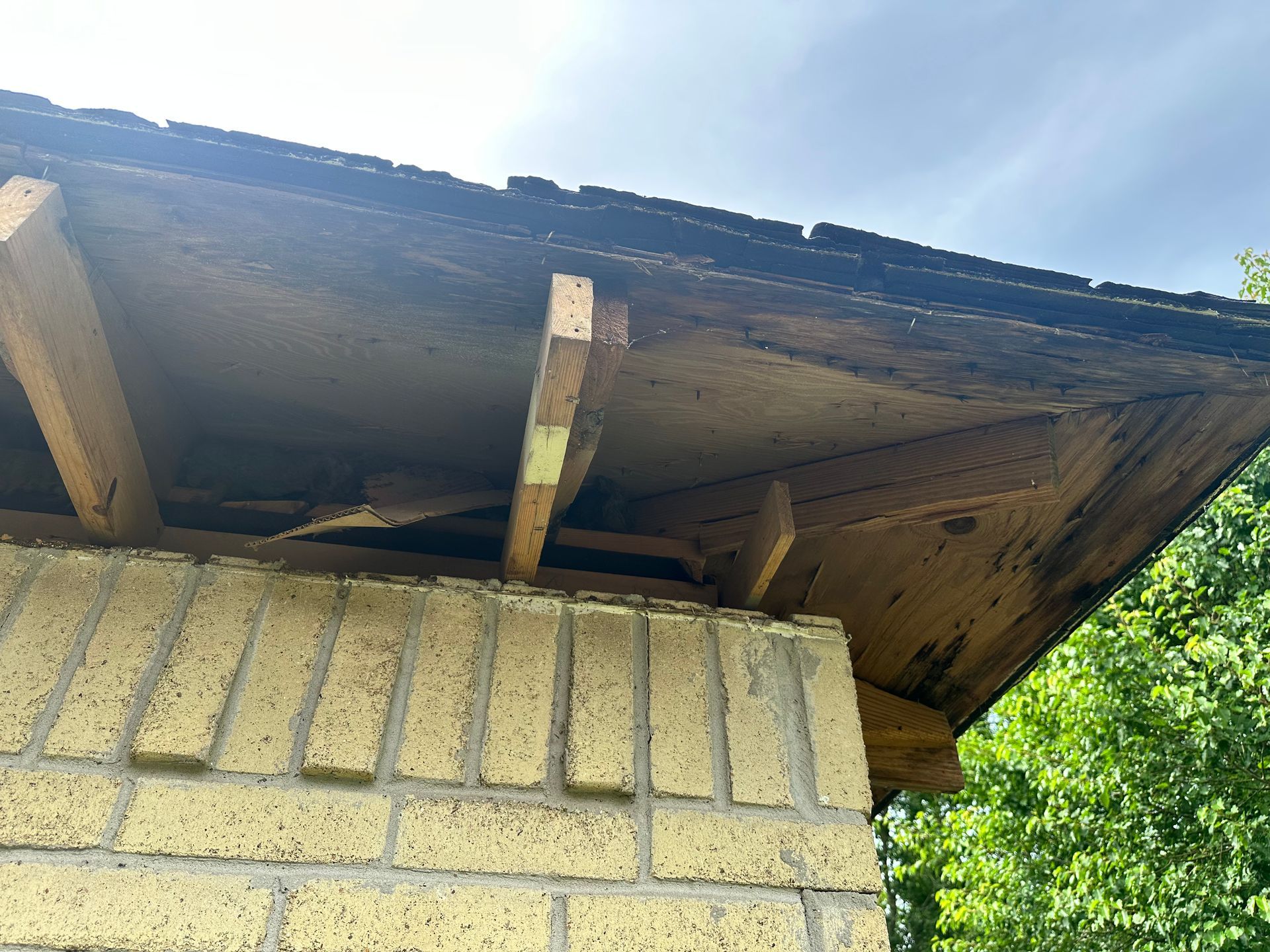 Brick wall with a damaged roof overhang, wooden beams, and a cloudy sky.