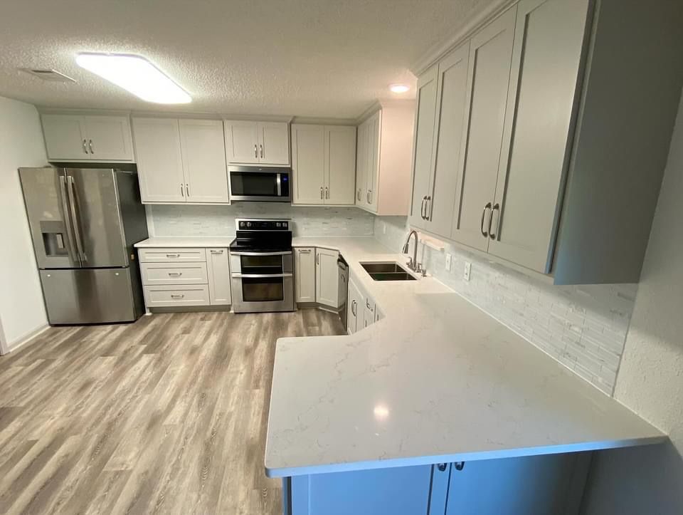 A kitchen with white cabinets , stainless steel appliances , a refrigerator and a sink.