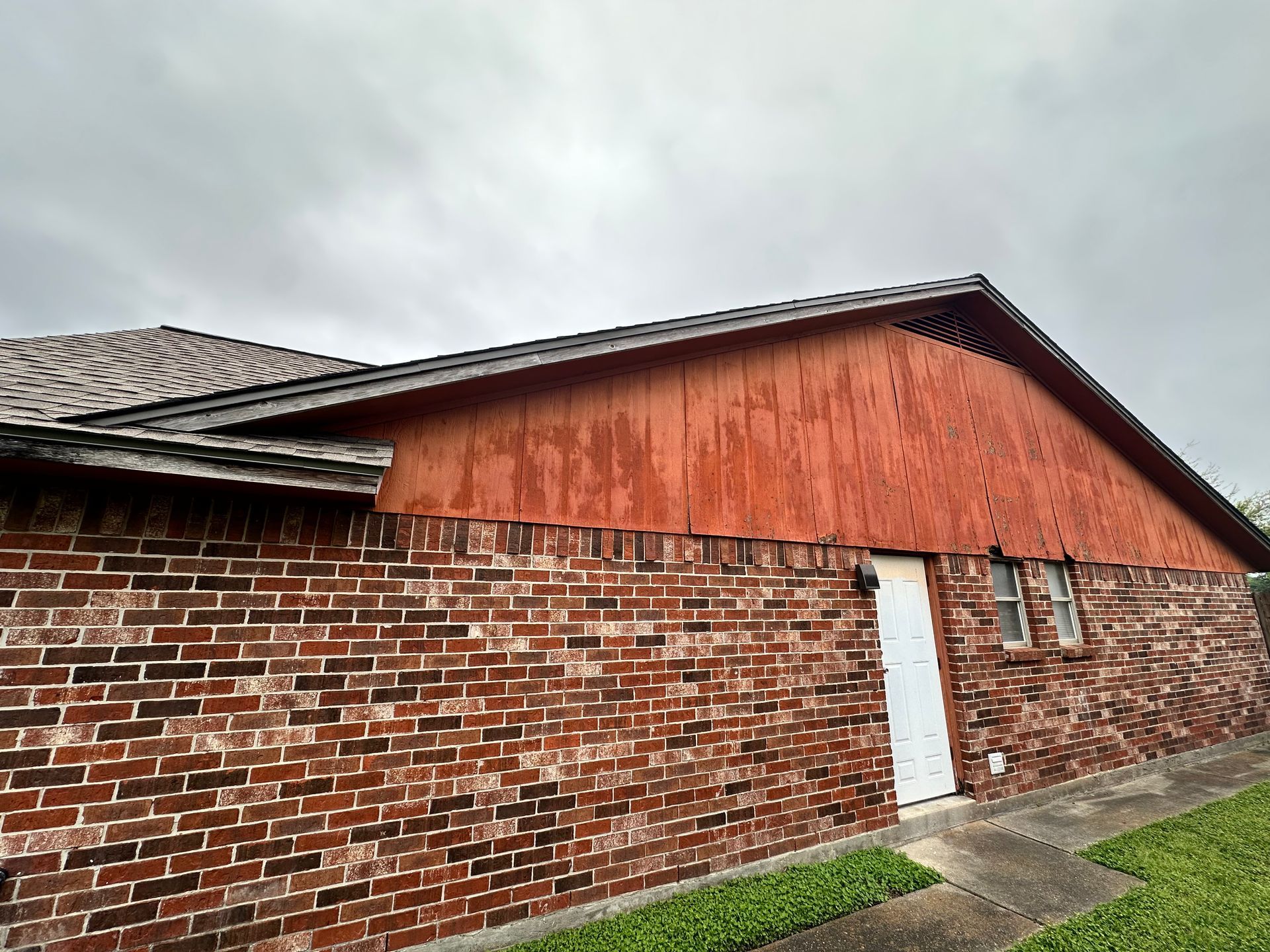 Brick building with a reddish-brown wooden gable. A door and small window are visible. Gray sky.