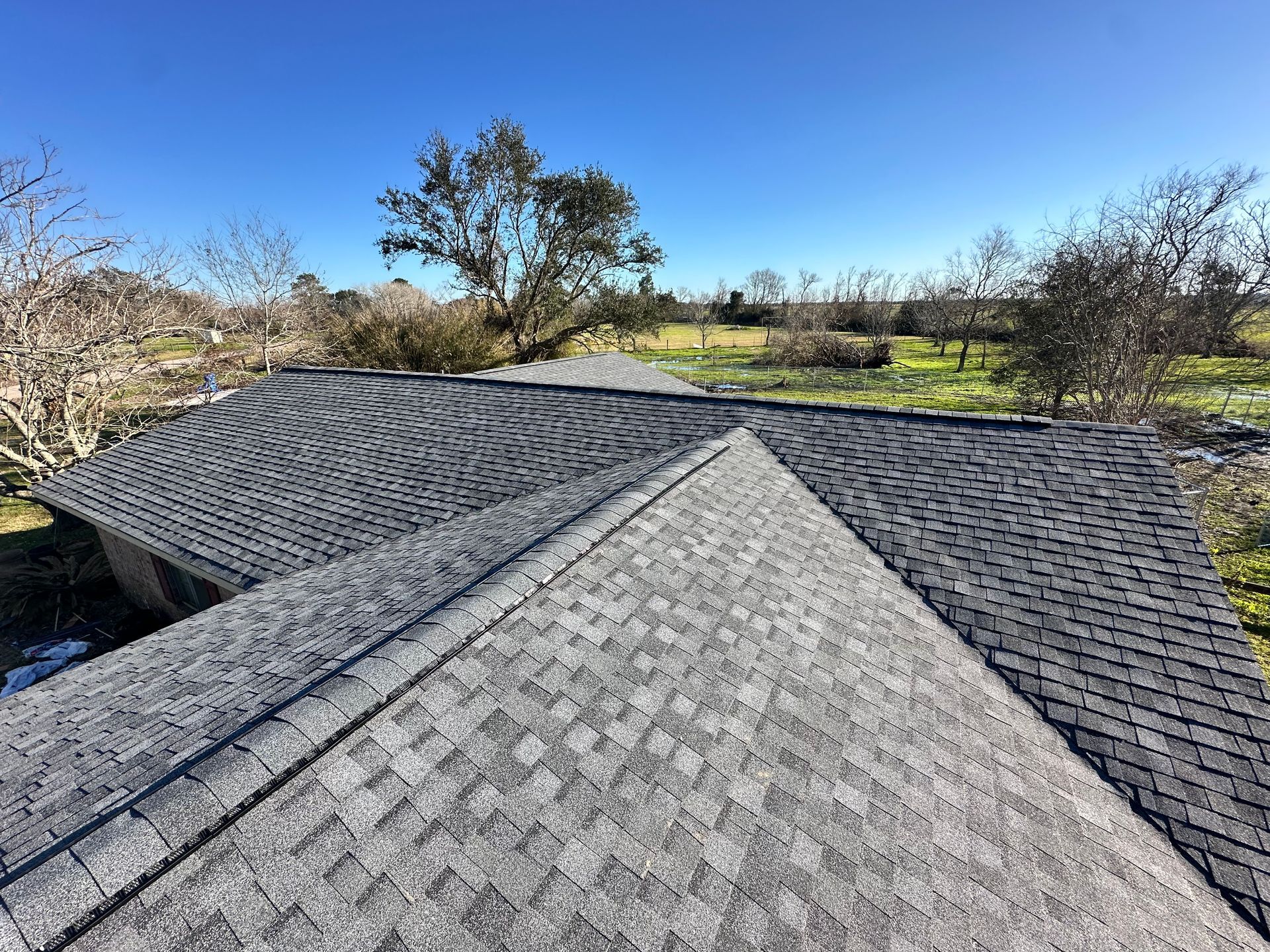 Dark gray shingle roof on a house, clear blue sky, sunny day.