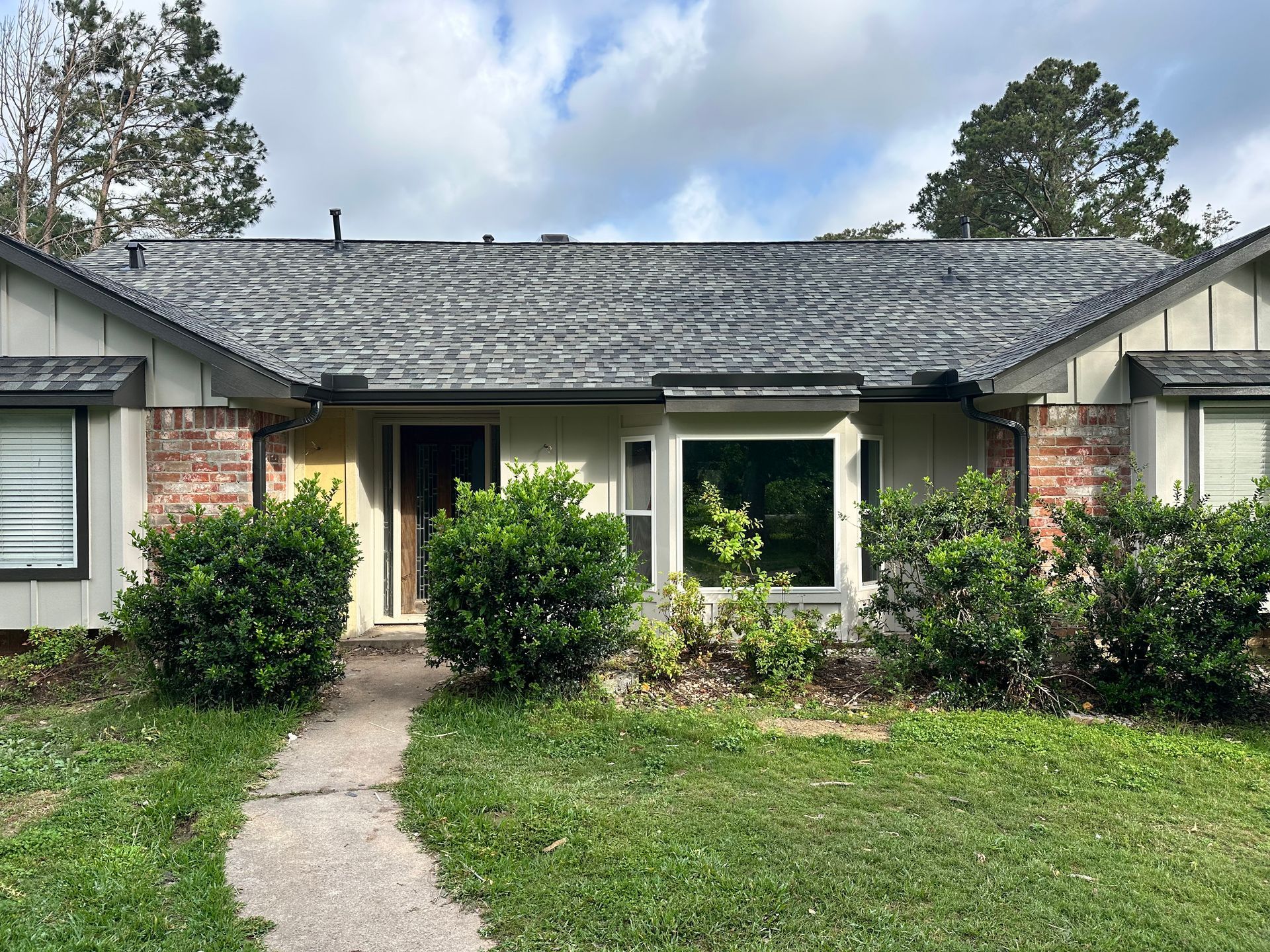 A light-colored house with a dark roof and a pathway leading to the front door. Bushes line the front.