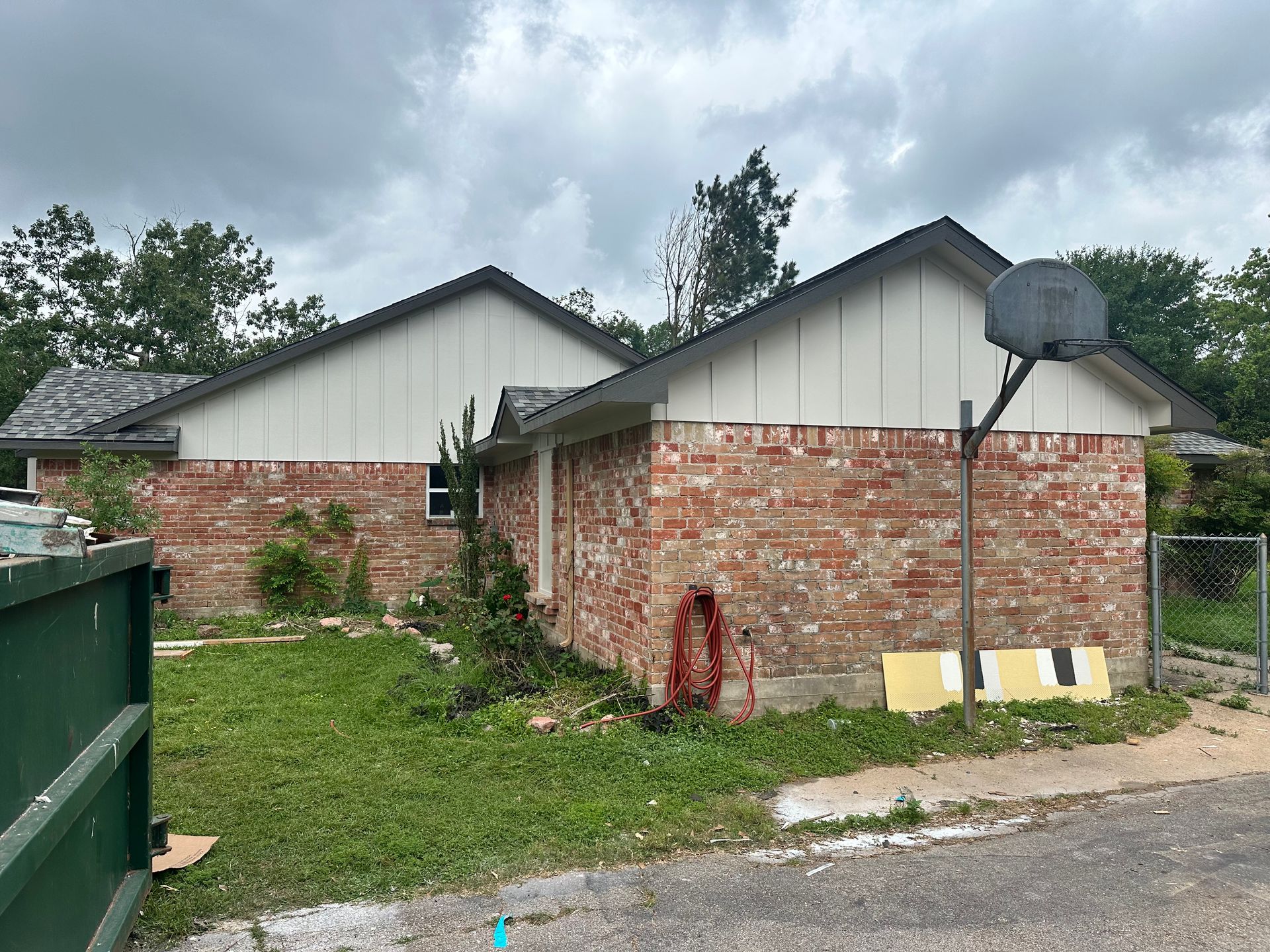 Brick house with white trim, gray roof, and a basketball hoop. Overcast sky.