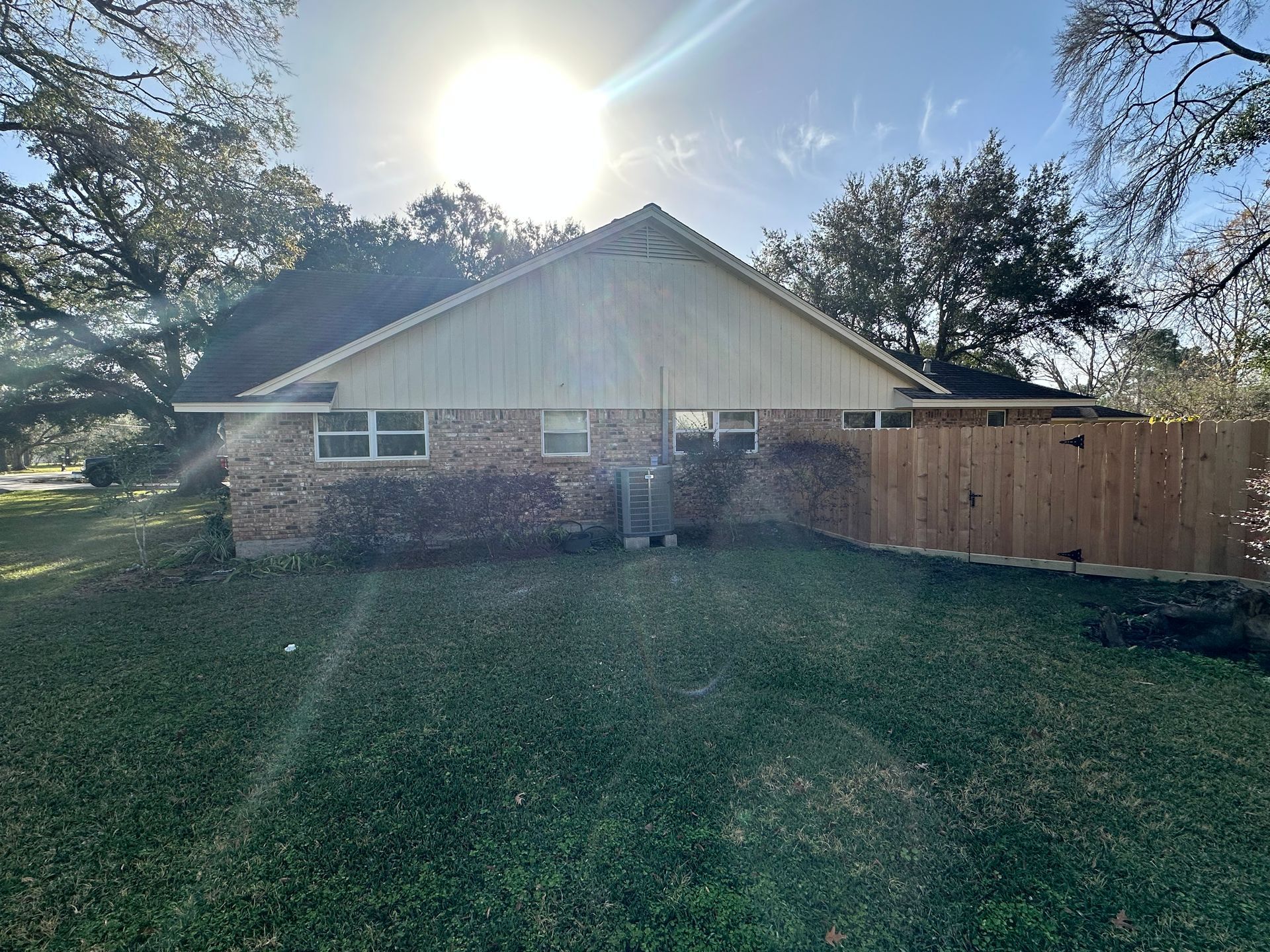 A brick house with a wooden fence and a bright sun in the background. Green grass in the foreground.