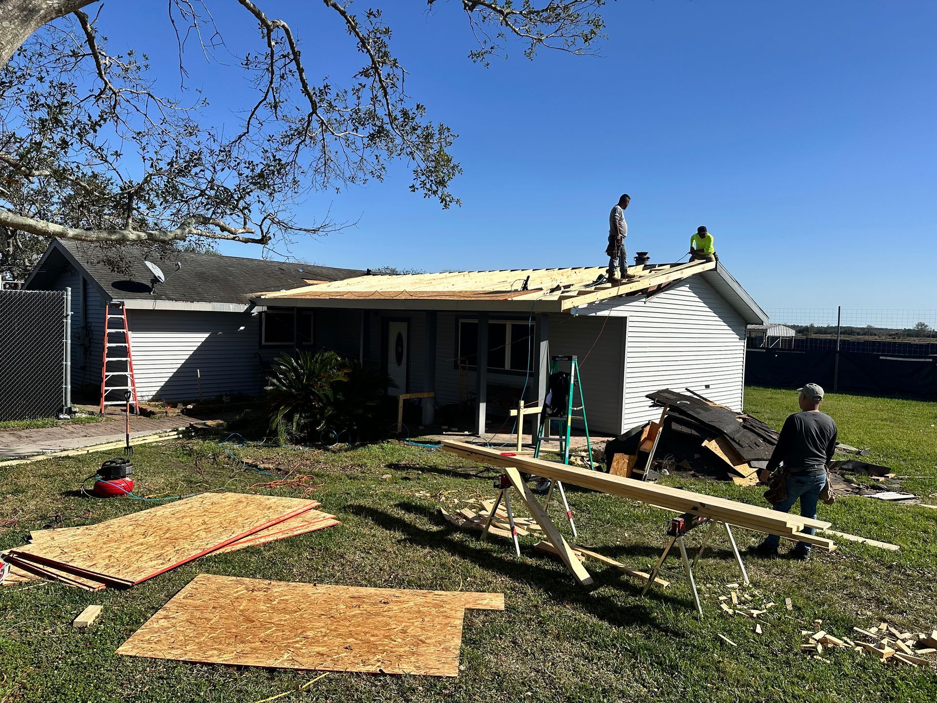 Workers installing a new roof on a small house, materials scattered on the ground.
