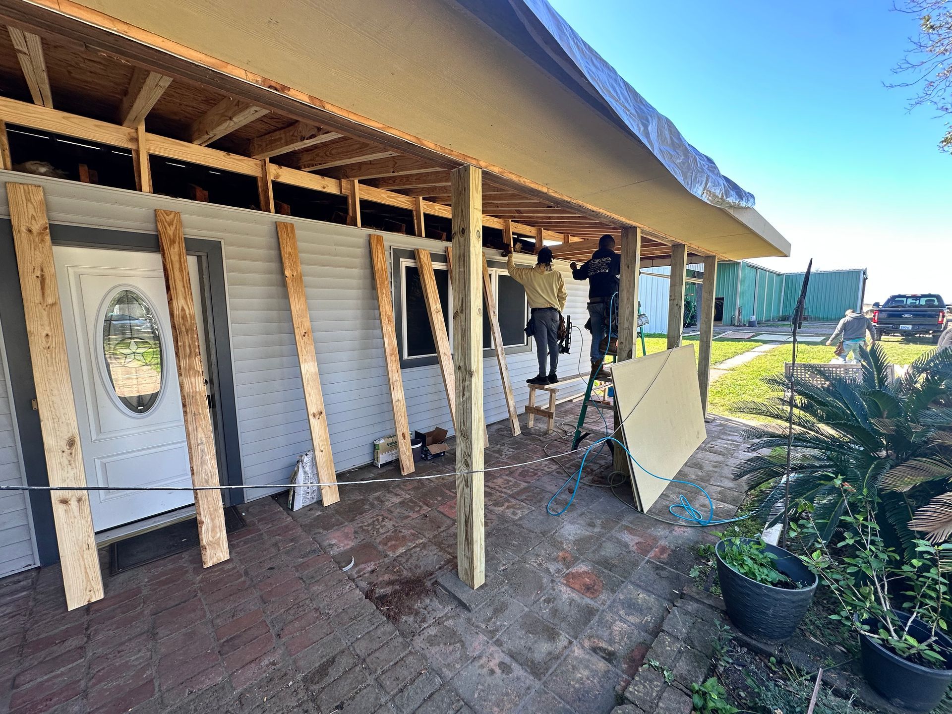 Construction workers renovating a house exterior, installing support beams and roofing materials.