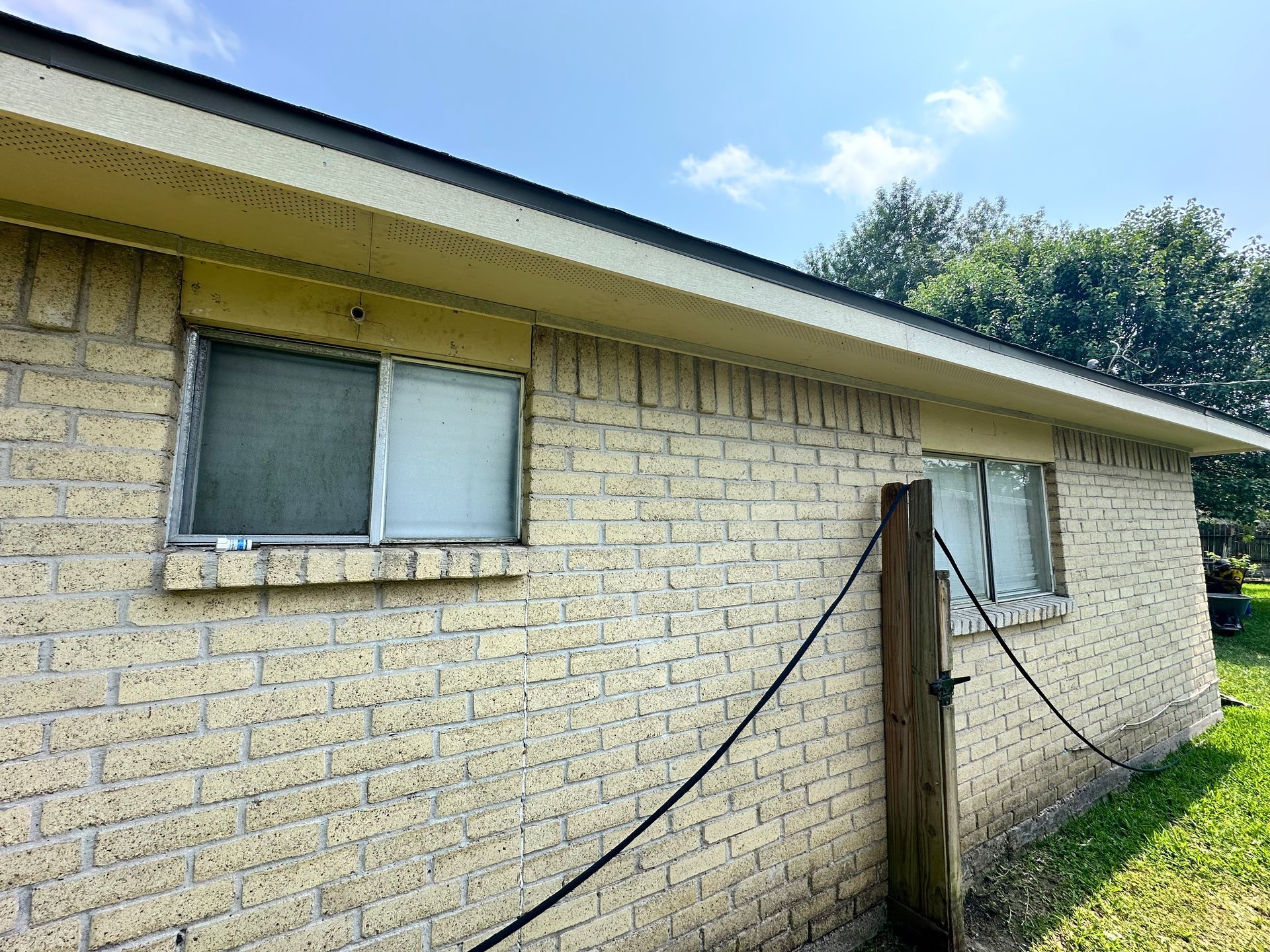 Brick building with two windows under a beige eave. A black cable runs to a wooden post.
