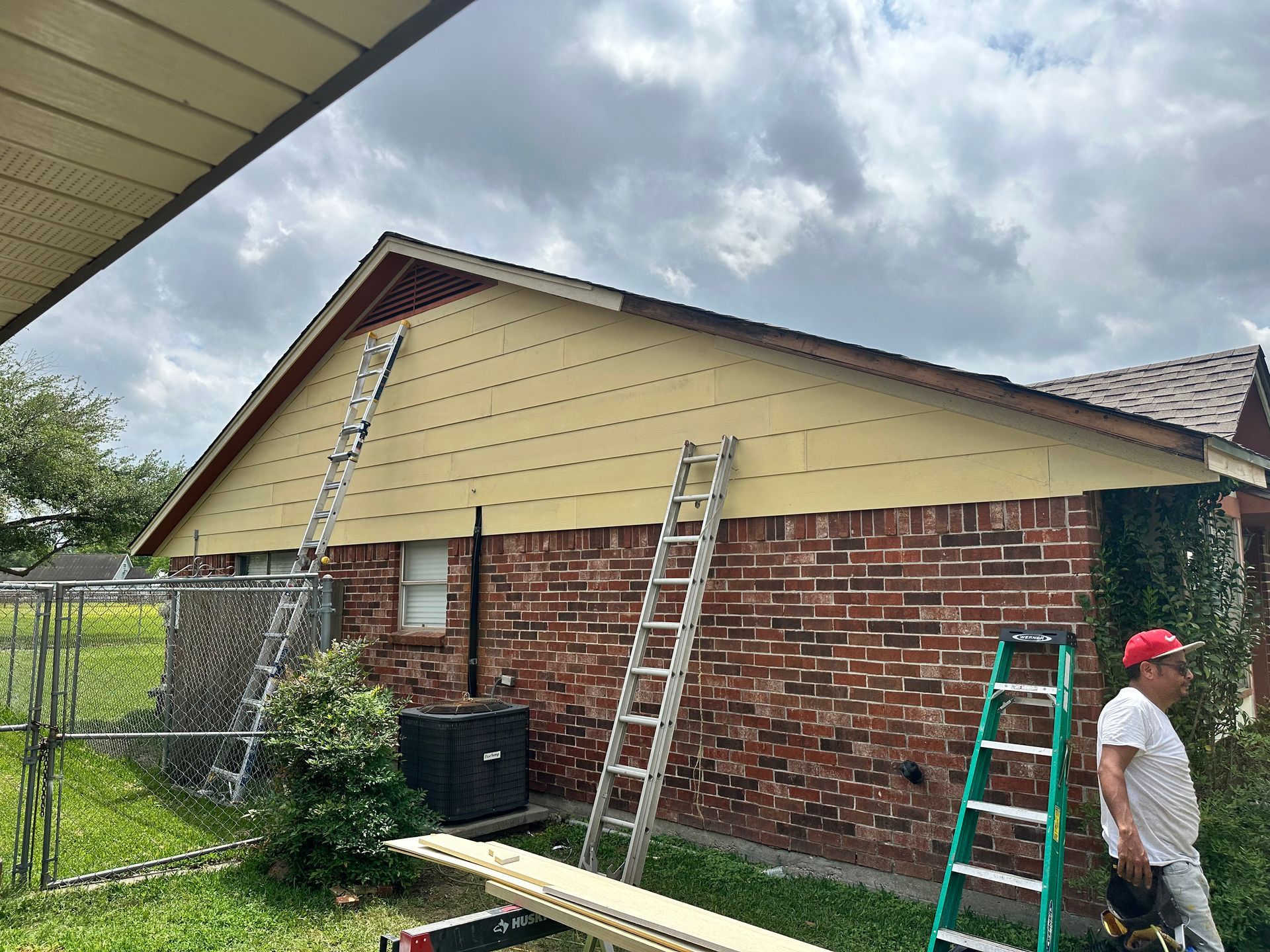 House exterior with ladders and person, yellow siding being installed over brick.