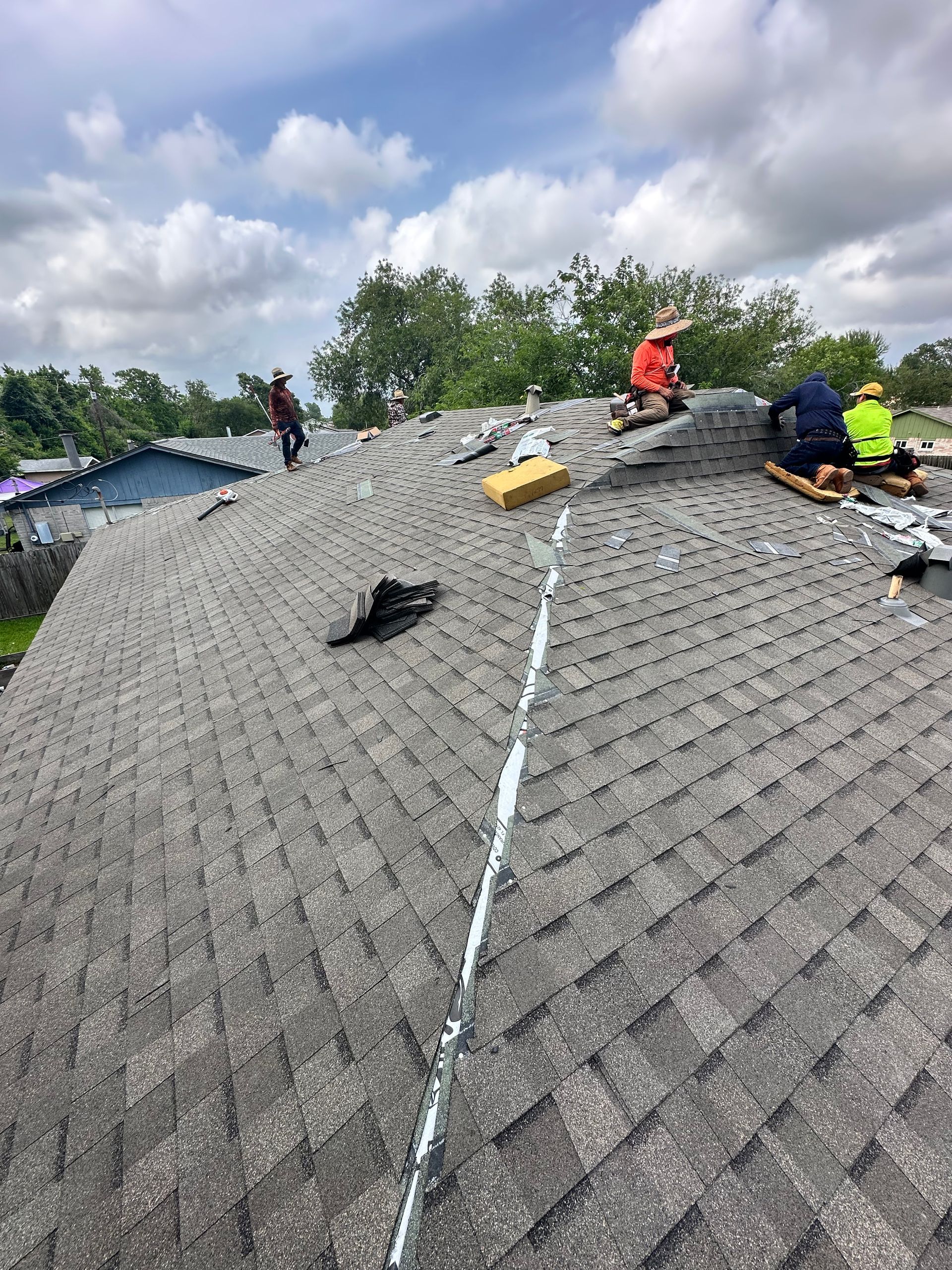 Roofers working on a shingled roof under a cloudy sky.