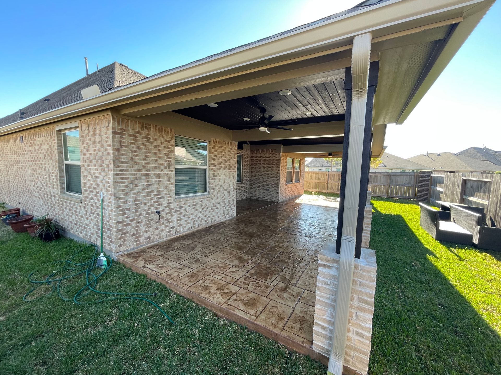 Brick home with covered patio, brown stamped concrete, and green grass.