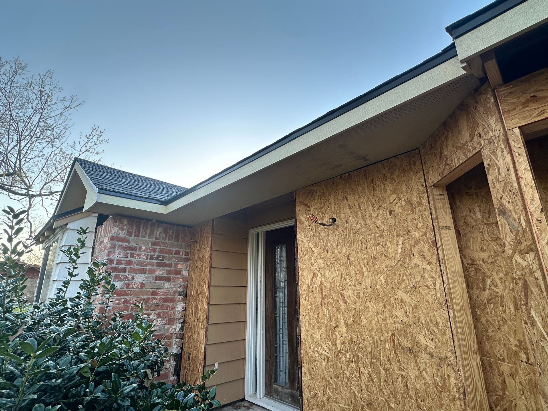 Exterior of a building under construction, showing exposed OSB, brick, and a partially finished roofline.
