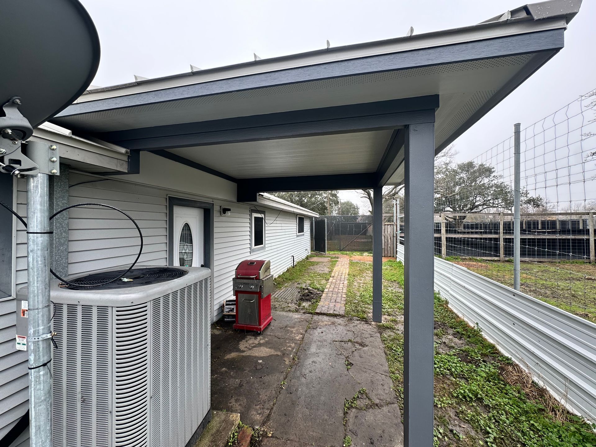 Exterior view of a house with a gray awning, air conditioning unit, and a metal fence.