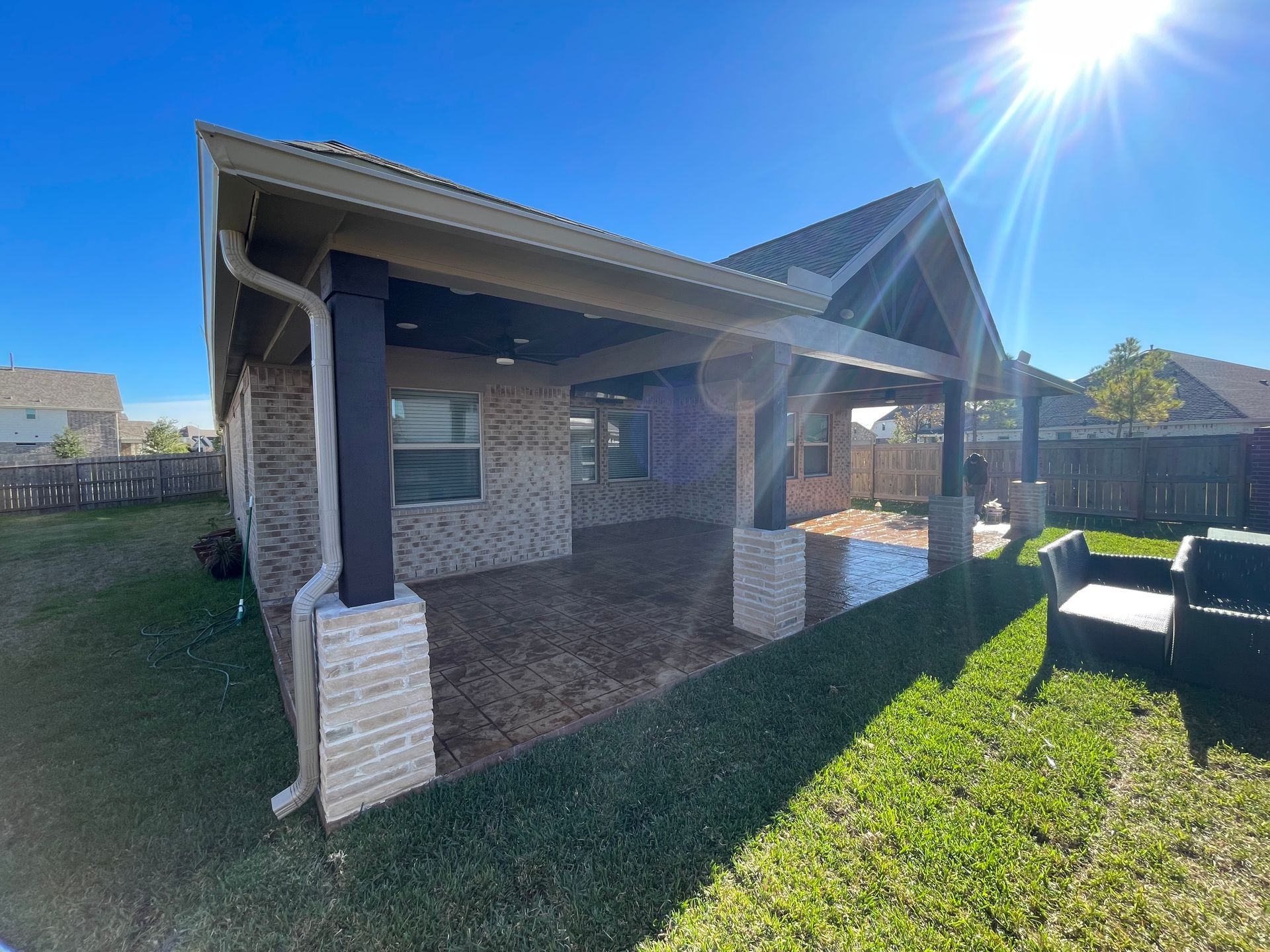 A covered patio with a brick wall and a shiny, wet floor, under a bright blue sky.