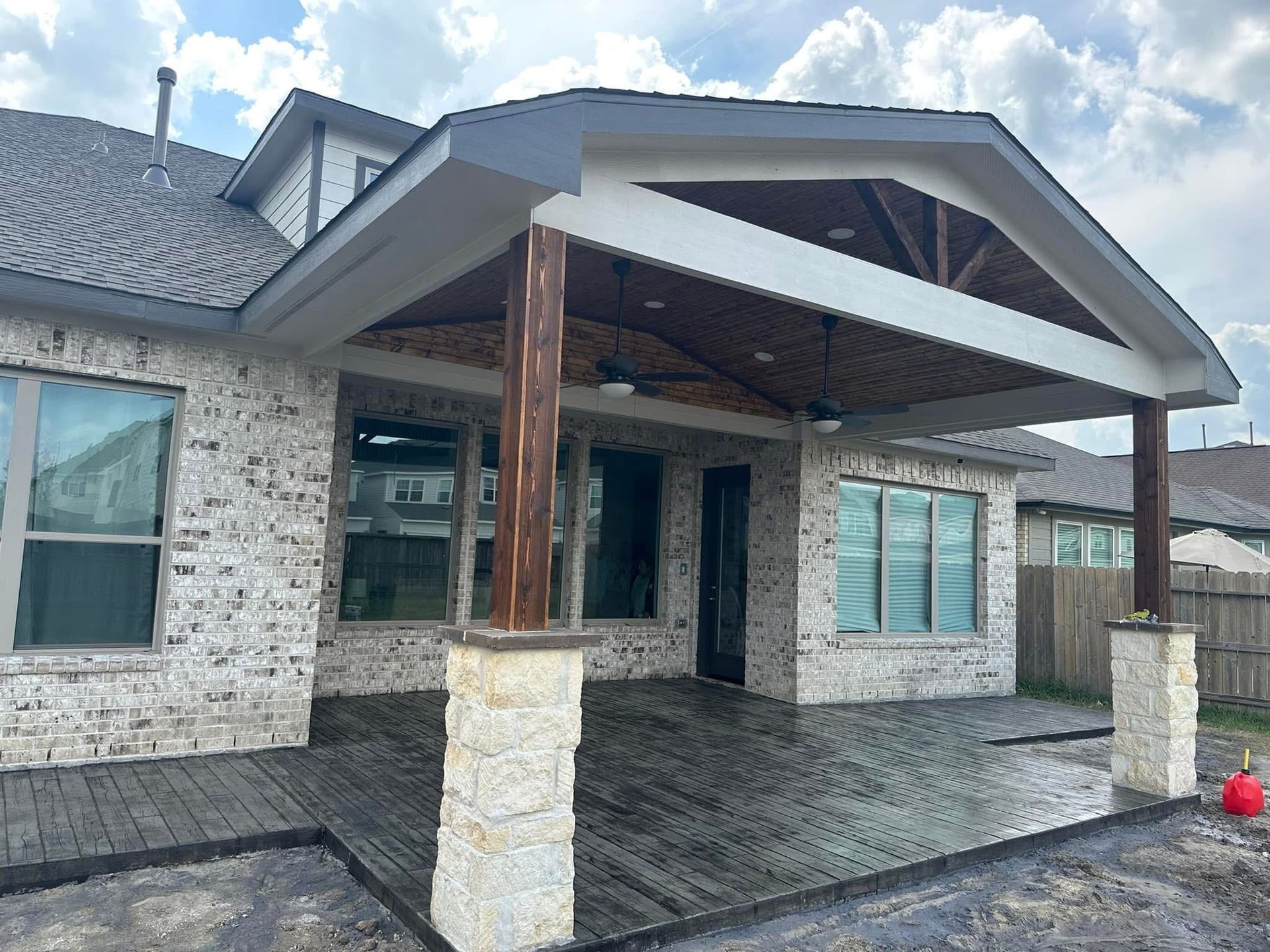 Backyard patio with wood and brick, covered with a gray roof and supported by columns.