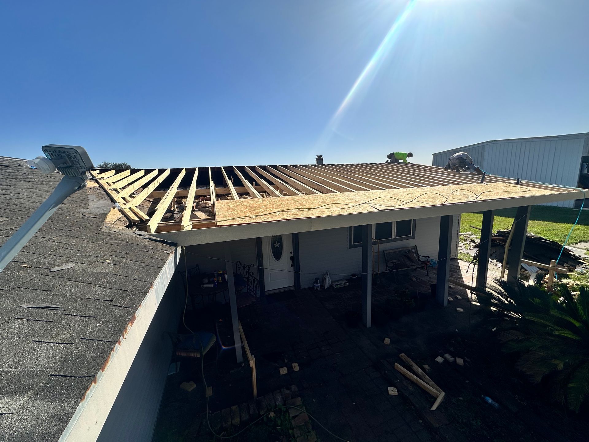 House roof partially under construction; wooden beams and plywood visible, bright sunny sky.