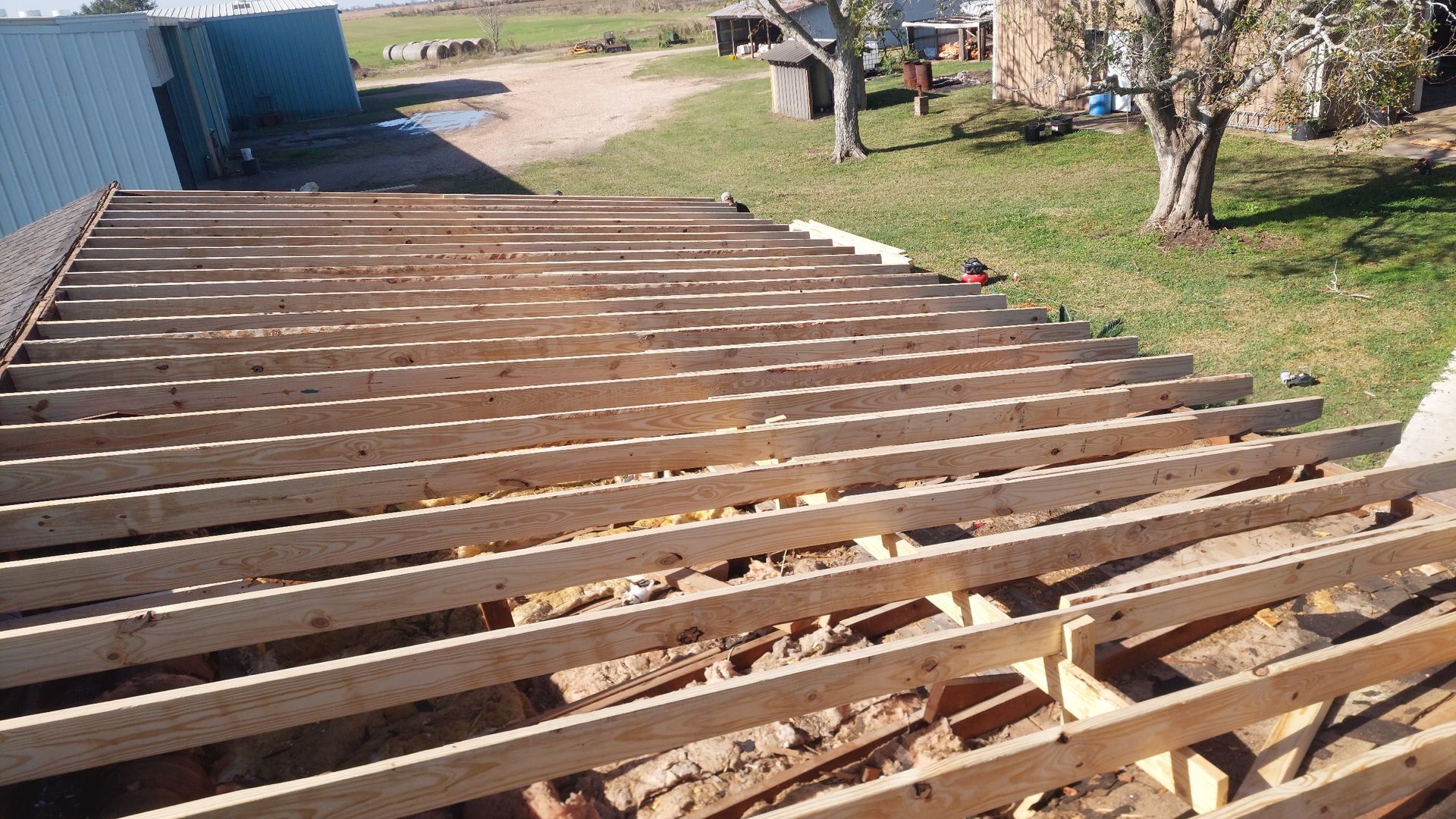 View of wooden roof rafters partially exposed, outdoors.