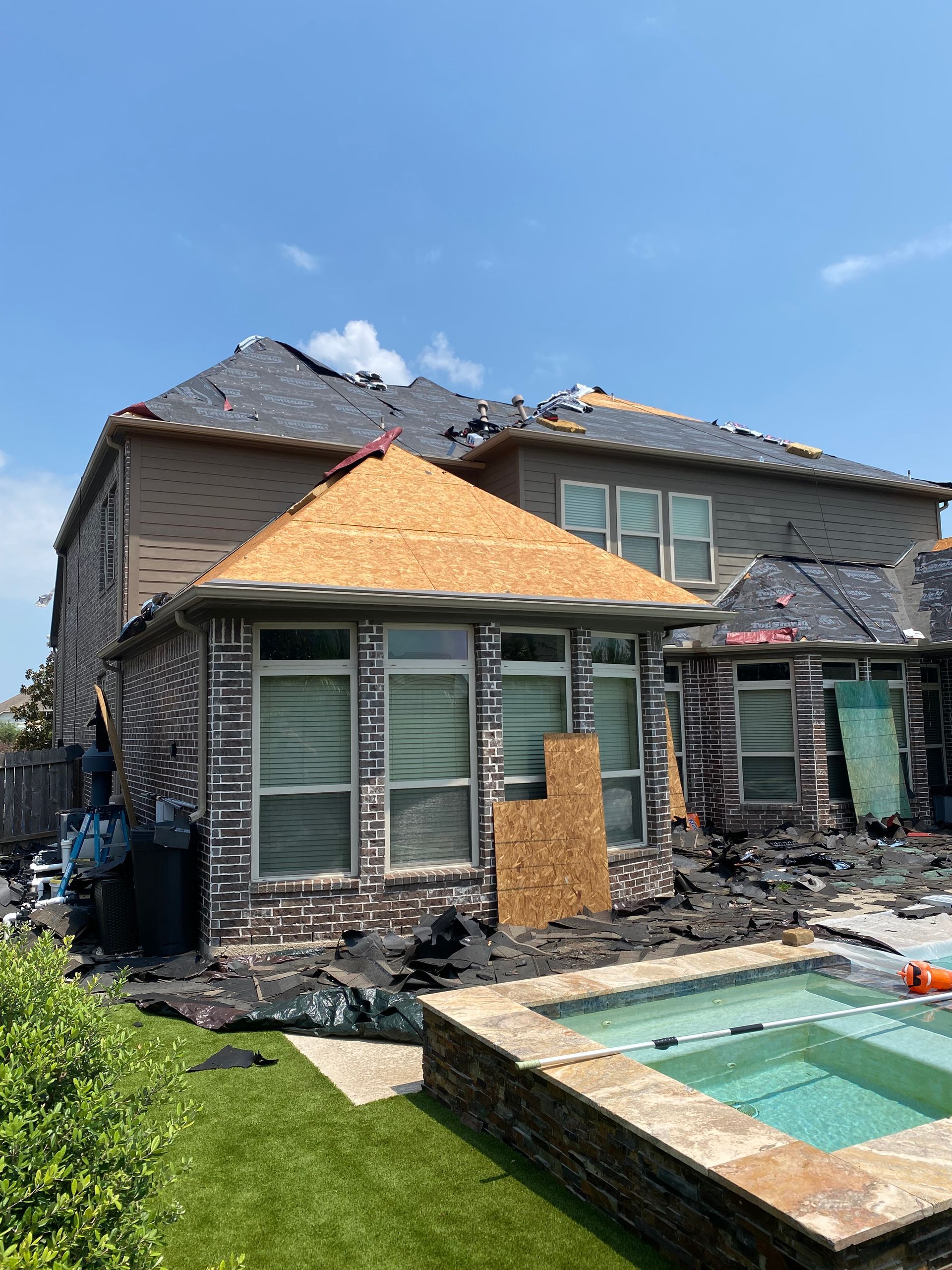 Damaged house after a storm with a partially destroyed roof and debris around a pool.
