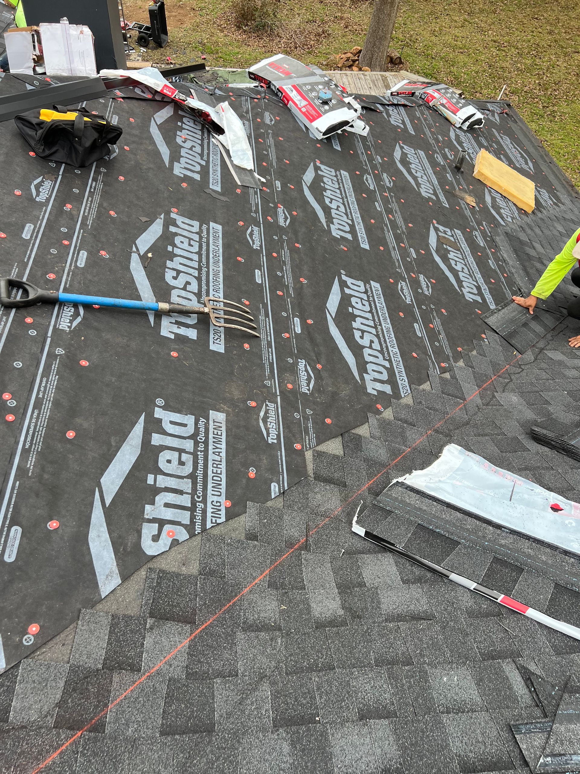 Roofer installing shingles over black roof underlayment labeled 